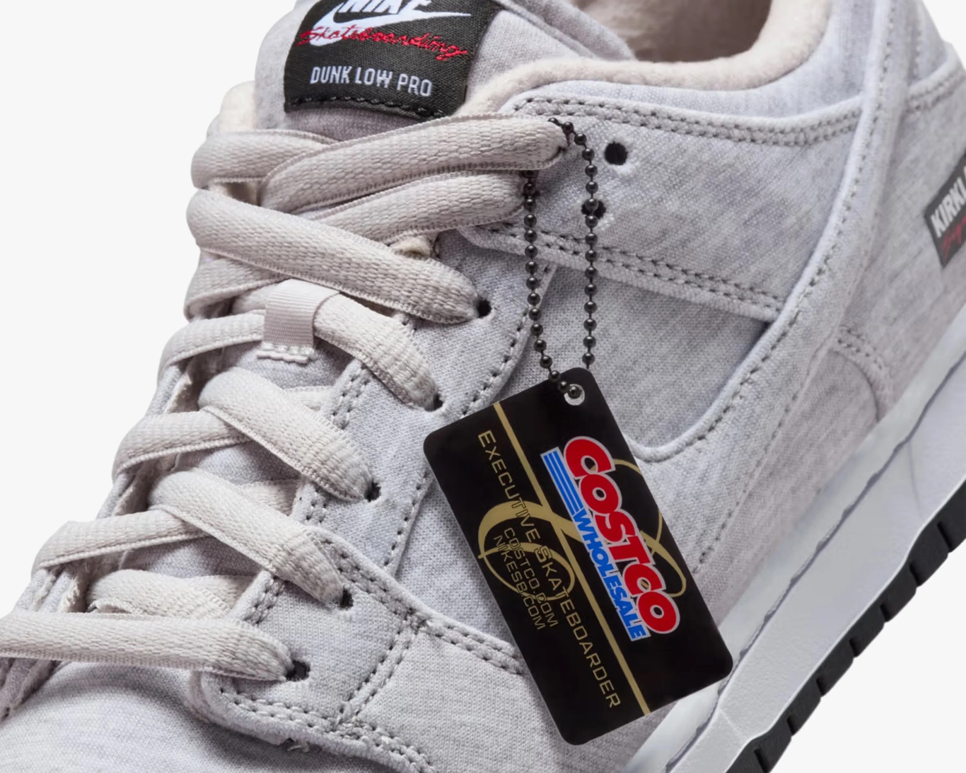 Close-up of a light gray Nike Dunk Low Pro sneaker with a Costco Wholesale hang tag attached to the laces.