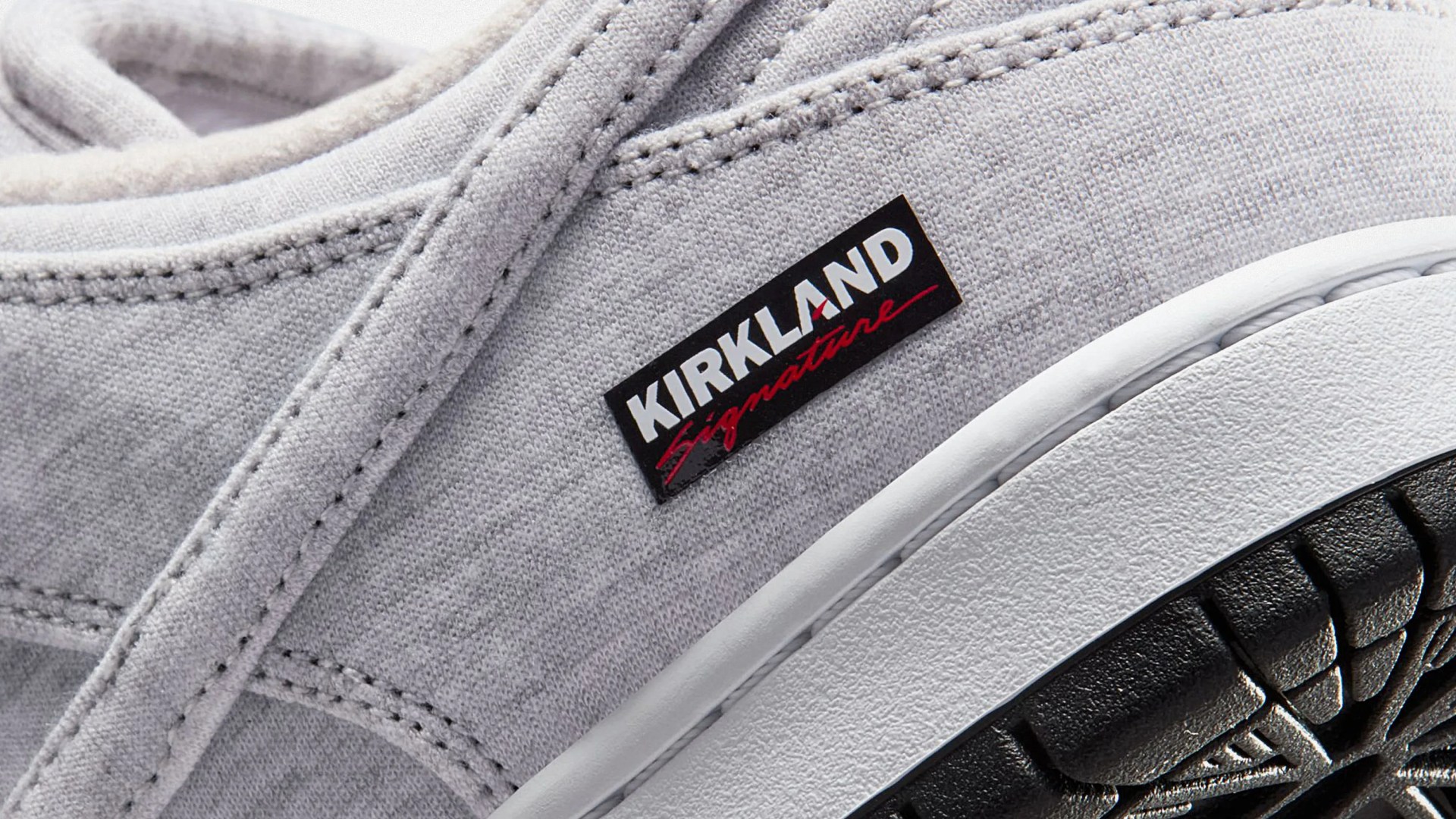 Close-up of a light gray fabric sneaker with a black and white "Kirkland Signature" label and a white midsole with a black textured outsole.
