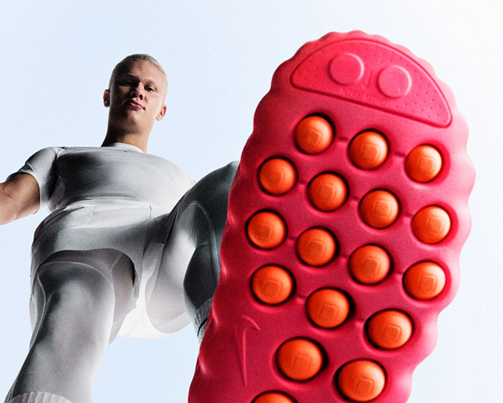 Person wearing white athletic clothing with one foot raised, showing the sole of a bright pink shoe with orange circular grips.