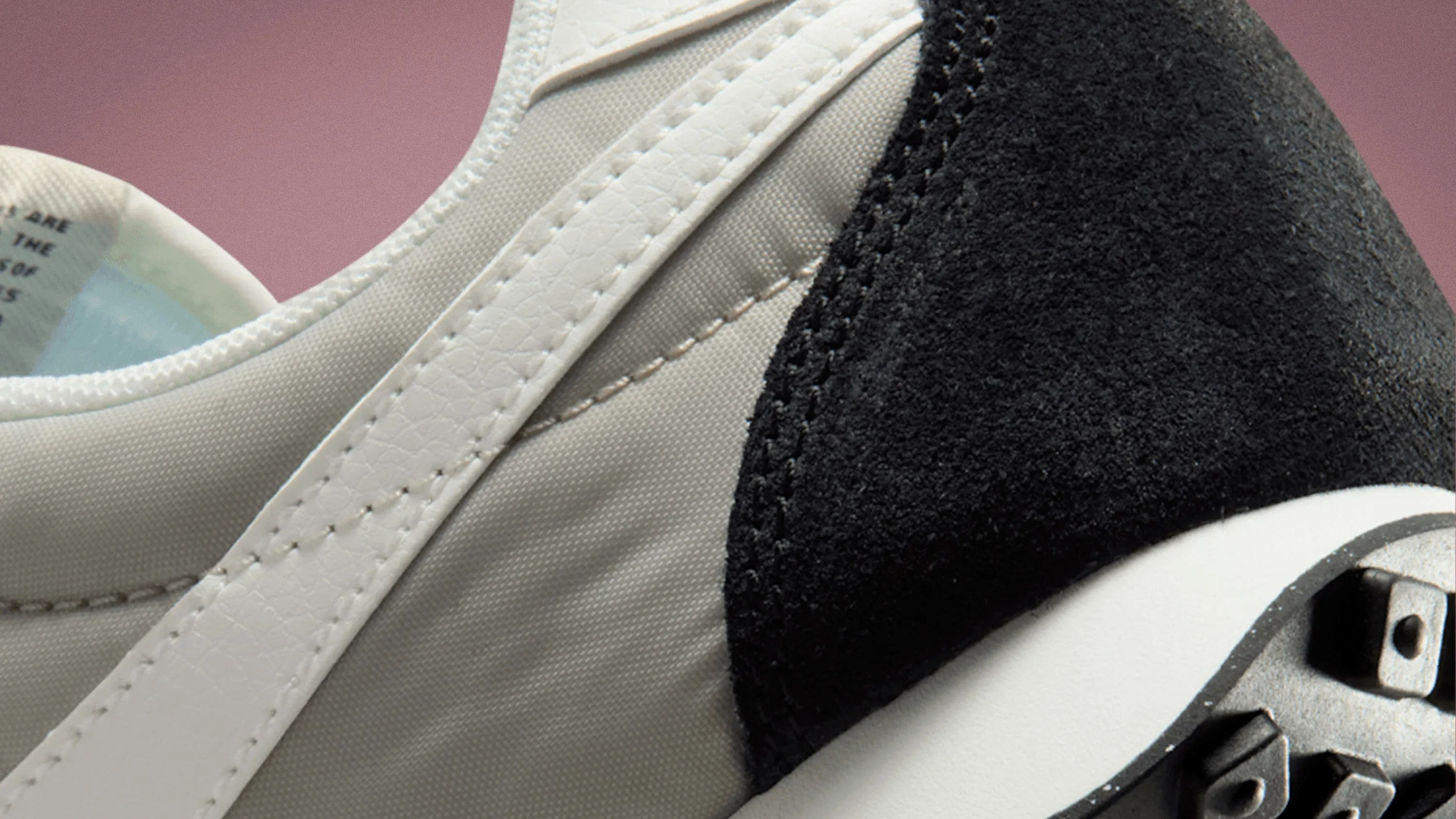 Close-up of a sneaker showing white leather trim, beige fabric upper, black suede heel, and part of a white sole with black studs.