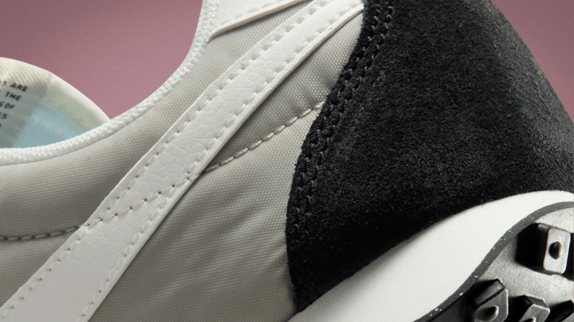 Close-up of a sneaker showing white leather trim, beige fabric upper, black suede heel, and part of a white sole with black studs.