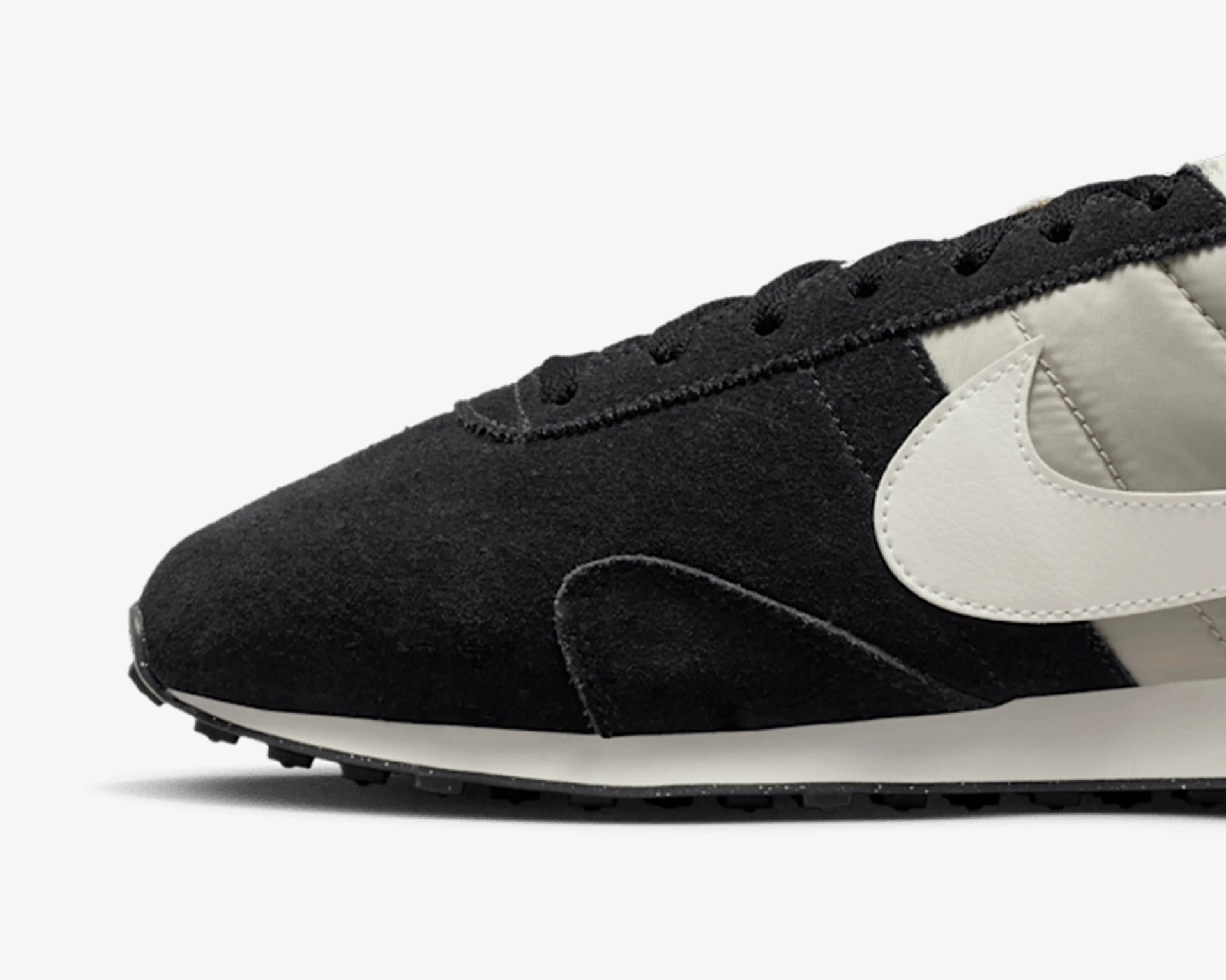 Close-up of black and beige Nike sneaker with white swoosh and black laces.