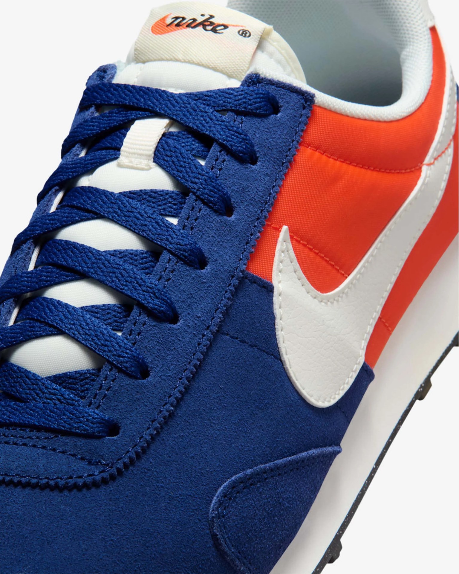Close-up of a Nike sneaker with blue suede, orange fabric, white swoosh, and blue laces.