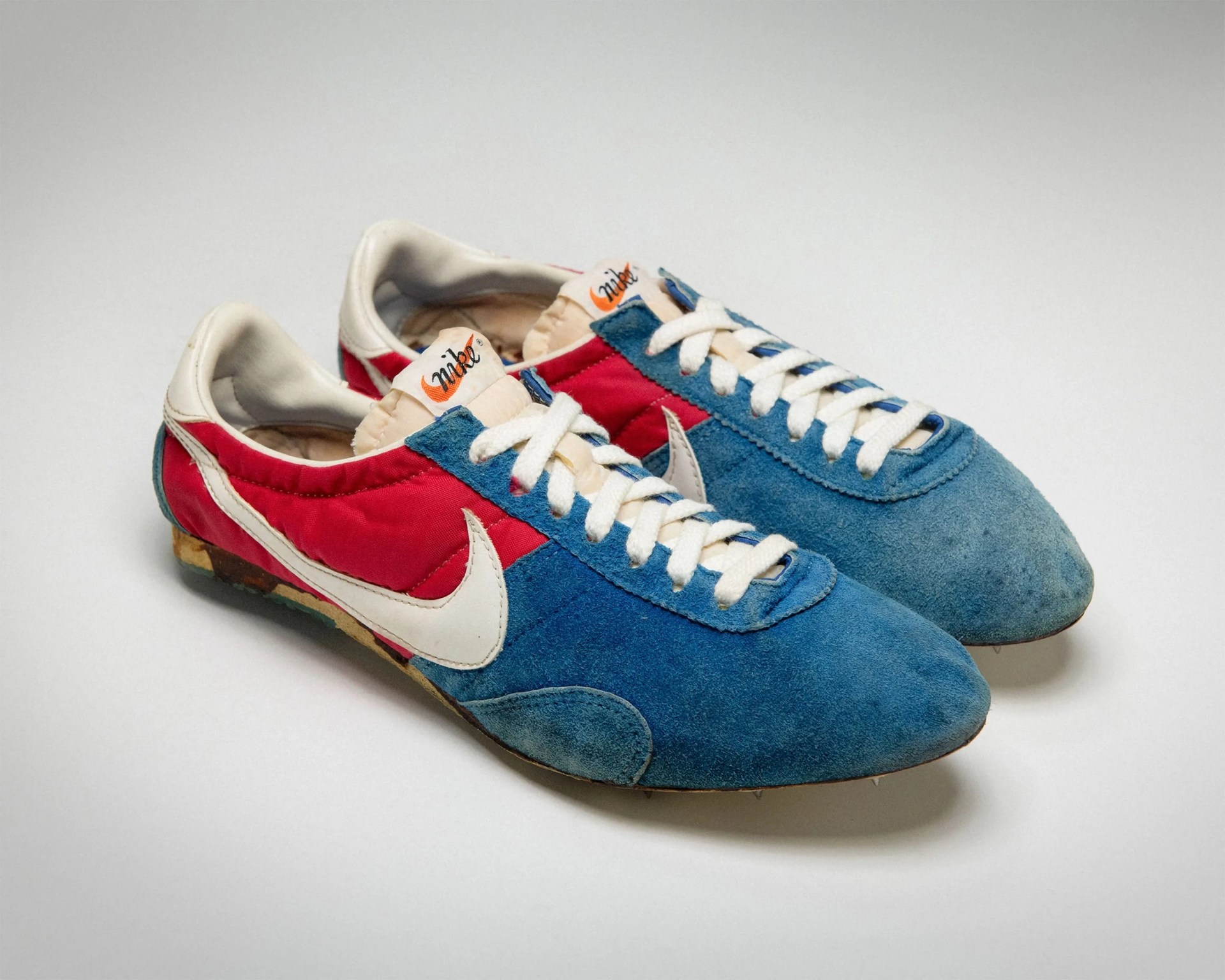 Pair of vintage Nike running shoes with blue suede toe, red nylon sides, white swoosh, and white laces.