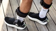 Black and white athletic shoes with white Nike socks and black ankle monitors on wooden floor.