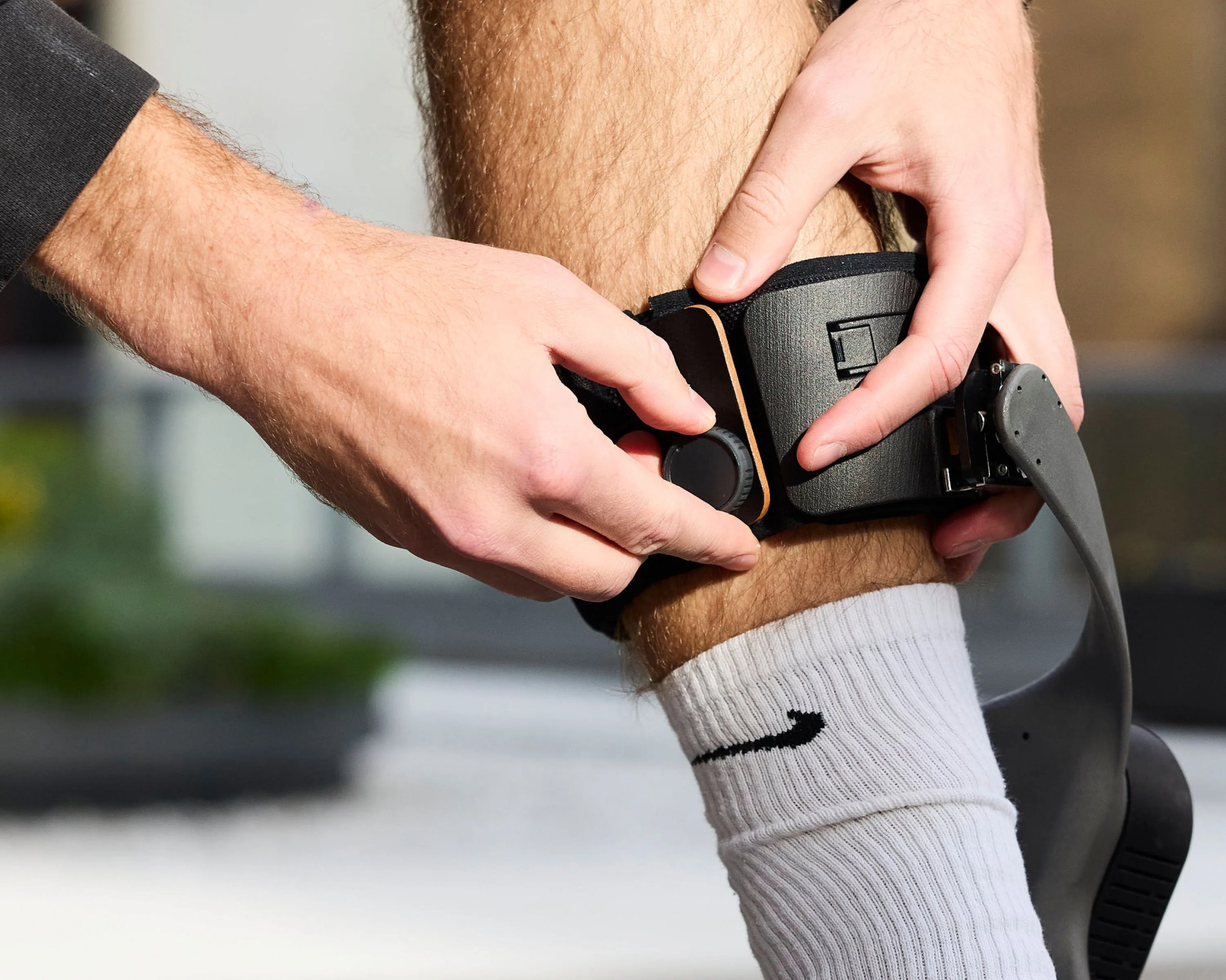 Black adjustable ankle brace with dial being fastened on a person's leg wearing a white Nike sock.