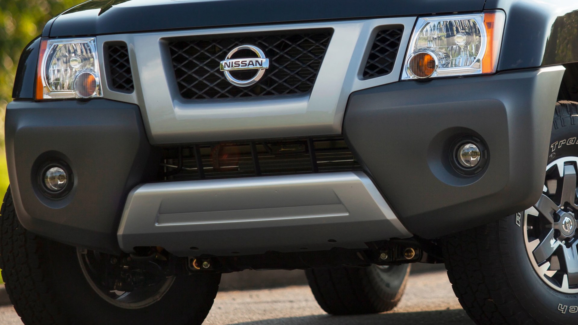Front view of a black Nissan SUV showing the grille, headlights, fog lights, and part of the tires.