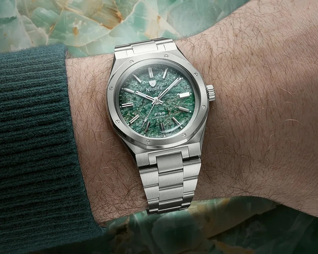 Silver stainless steel wristwatch with green textured dial and metal bracelet worn on a wrist.
