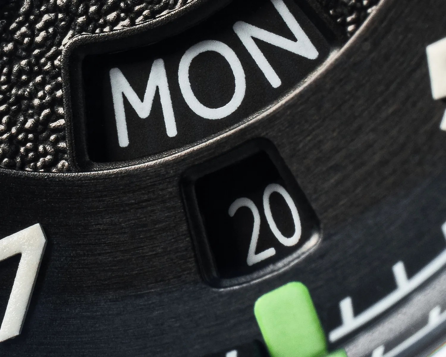 Close-up of a black watch dial showing the day "MON" and date "20" in white text.
