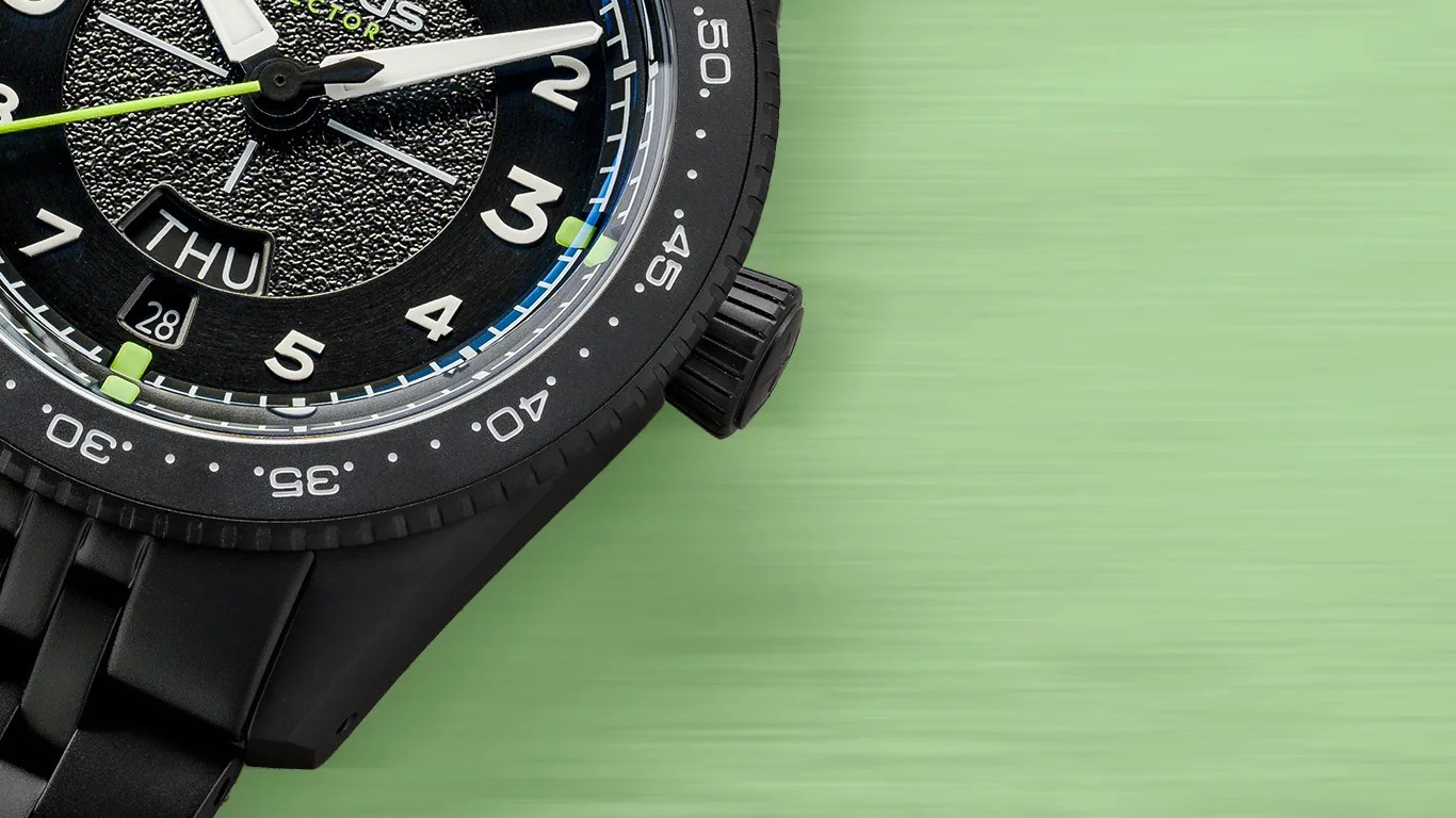 Close-up of a black wristwatch with white numerals, a textured dial, day and date display, and a black metal band on a green surface.