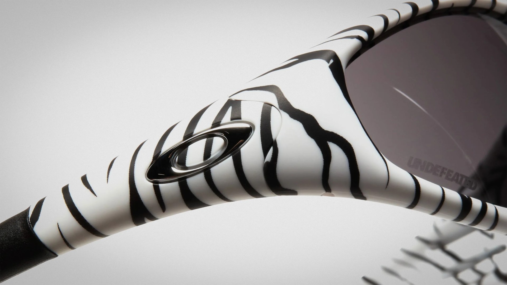 Close-up of white sunglasses with black zebra stripes and a black Oakley logo on the arm.