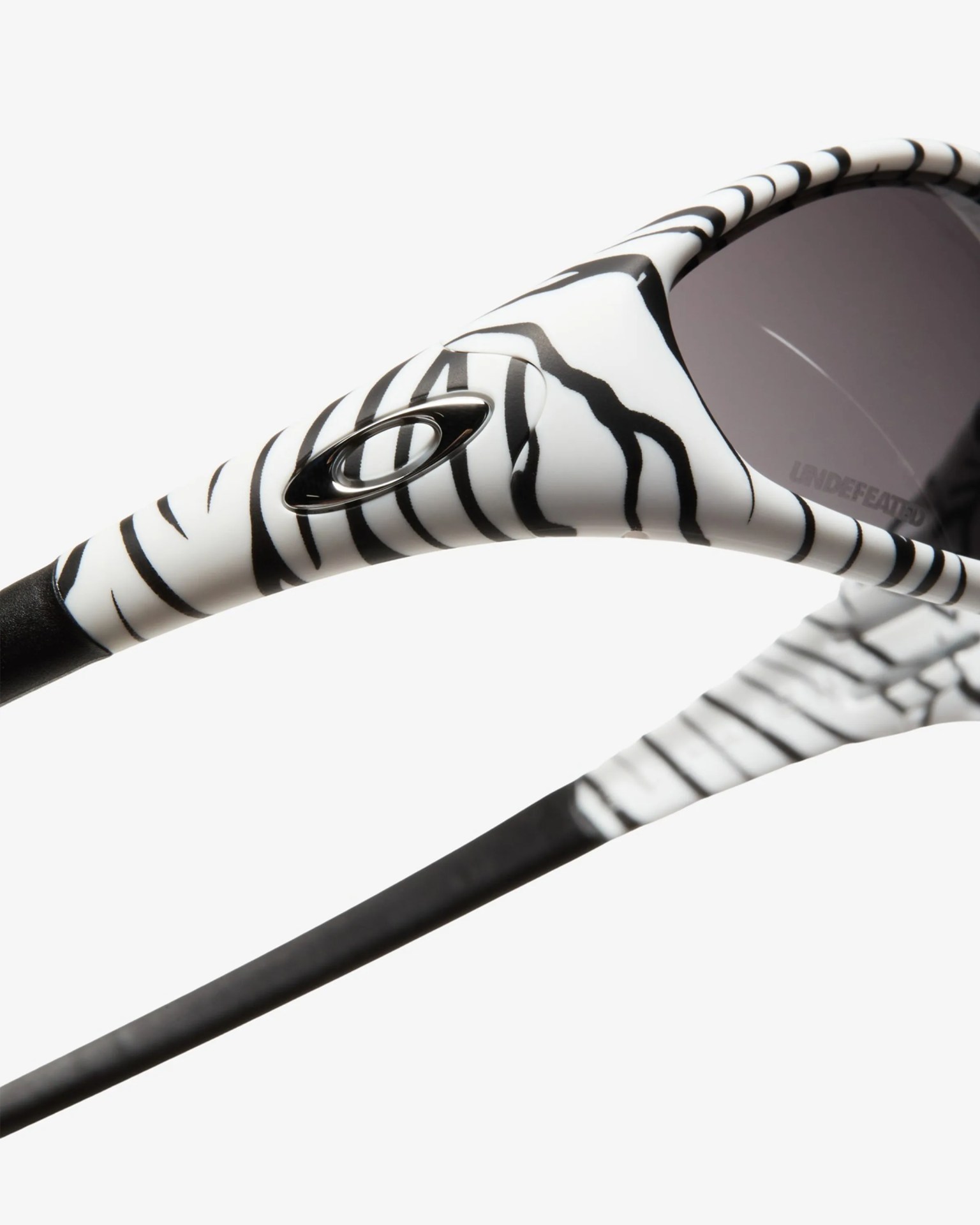 Close-up of white sunglasses arm with black zebra stripes and a black Oakley logo.