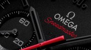 Close-up of a black Omega Speedmaster watch face with red and black hands and white markings.