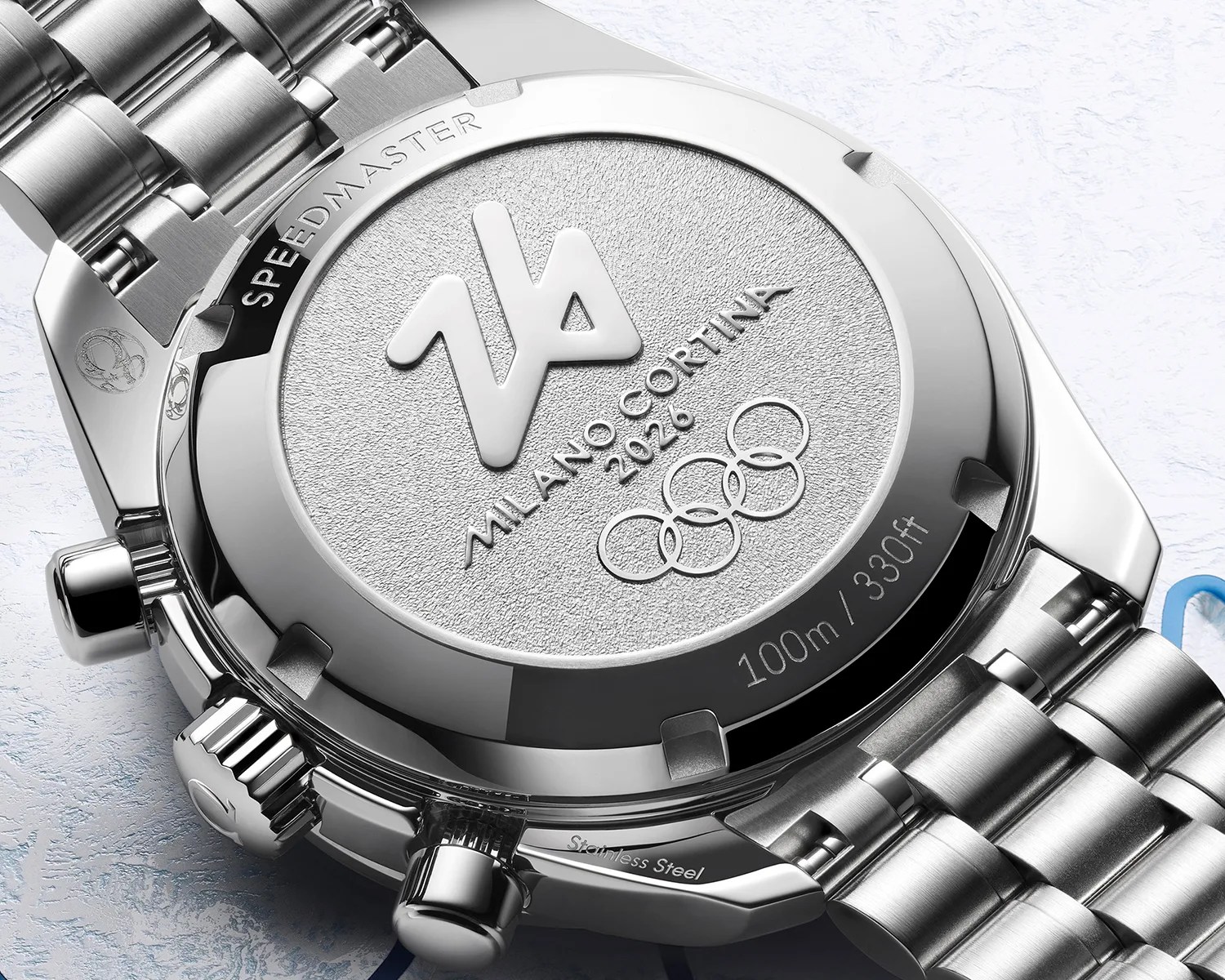 Close-up of the stainless steel back of a Speedmaster watch engraved with "Milano Cortina 2026" and Olympic rings.