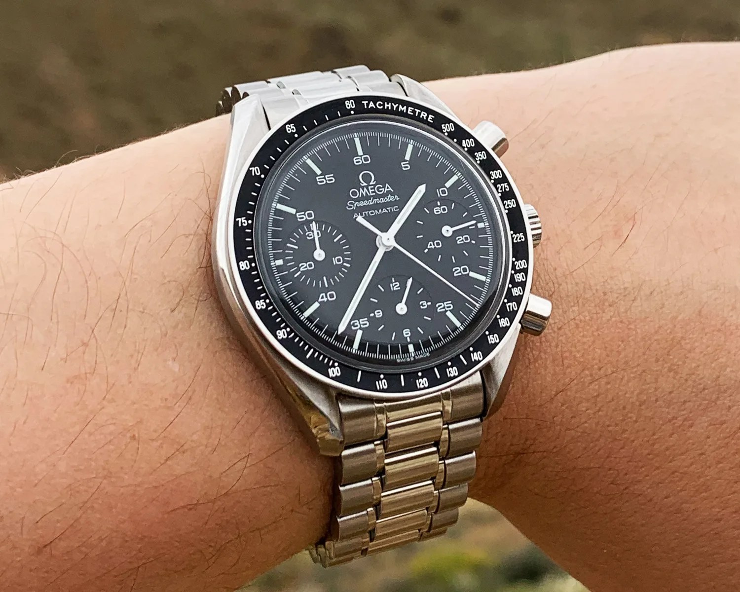 Omega Speedmaster Automatic wristwatch with black dial and stainless steel bracelet worn on a wrist.