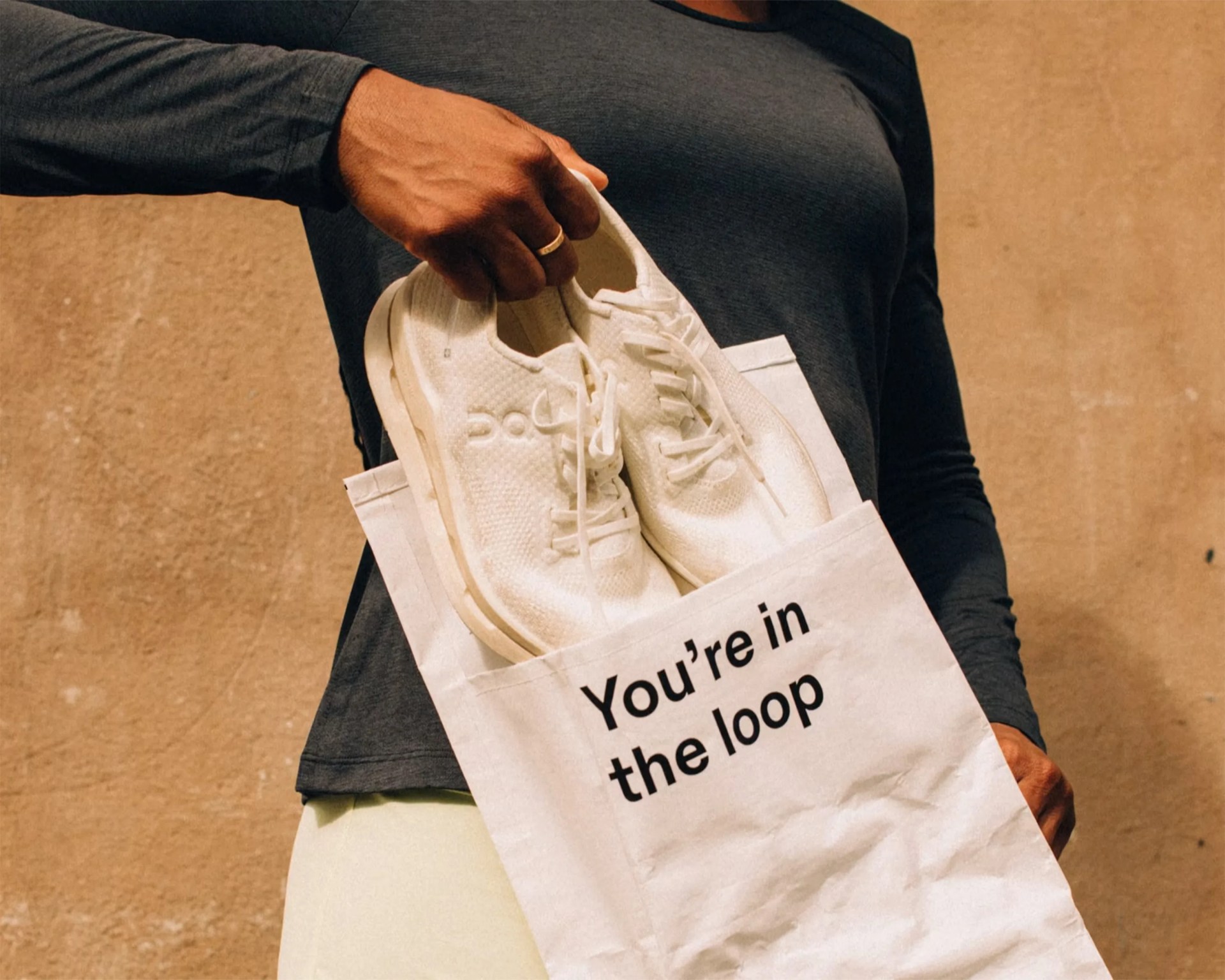 Person holding white sneakers in a white tote bag with "You're in the loop" text.