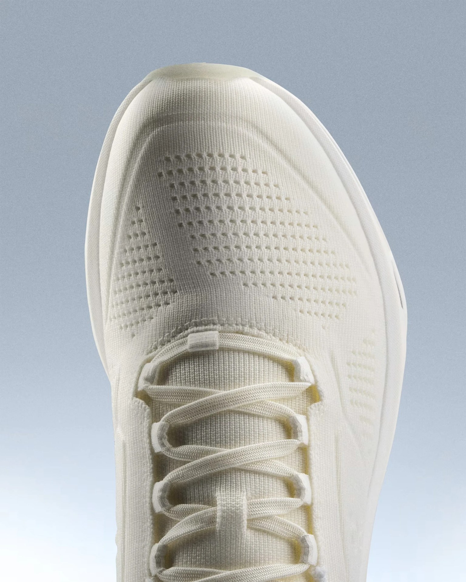 Close-up of the top front of an off-white knit sneaker with matching laces and a textured pattern on the toe area.