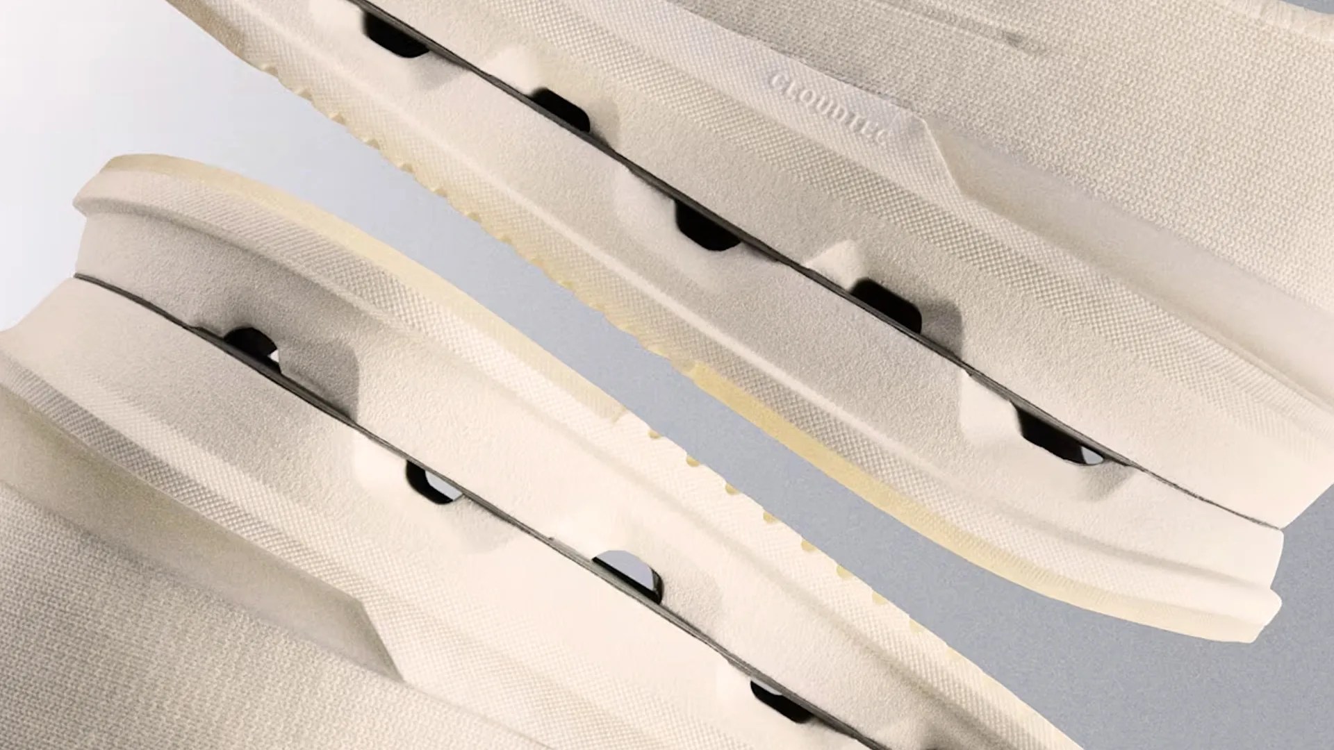 Close-up of beige sneakers with thick textured soles featuring black cutout details and the word "GROUND" embossed.
