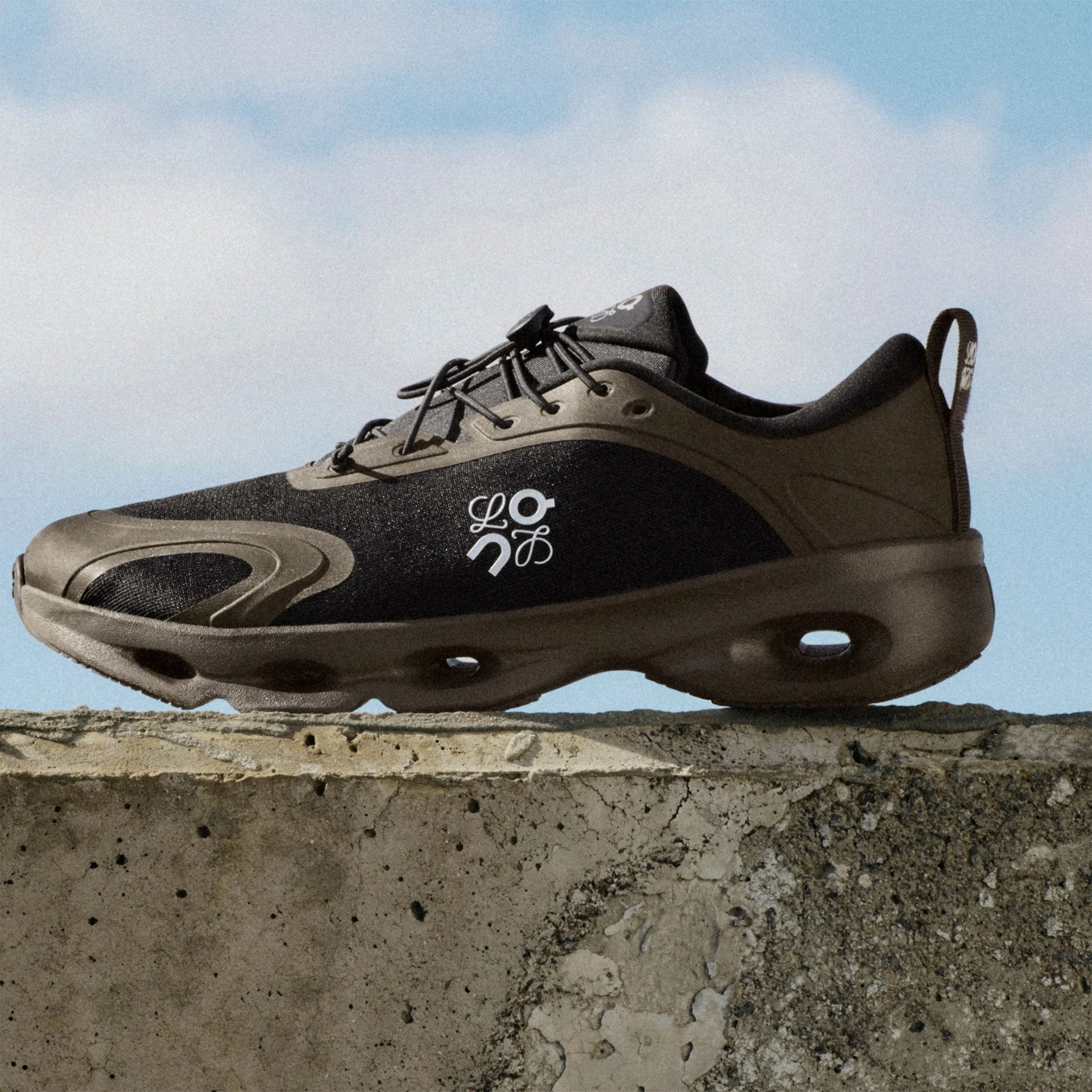Black and brown athletic sneaker with white logo and unique sole design on a concrete ledge against blue sky.