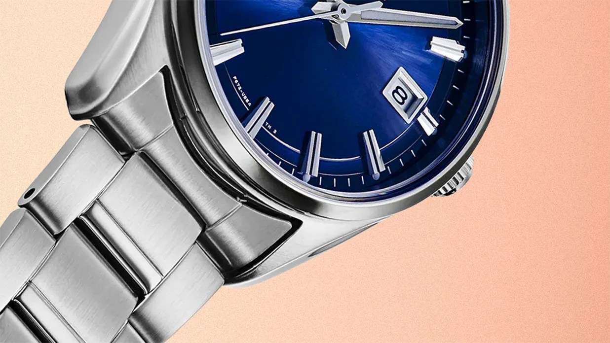 Close-up of a stainless steel wristwatch with a blue dial and a date window showing the number 8.