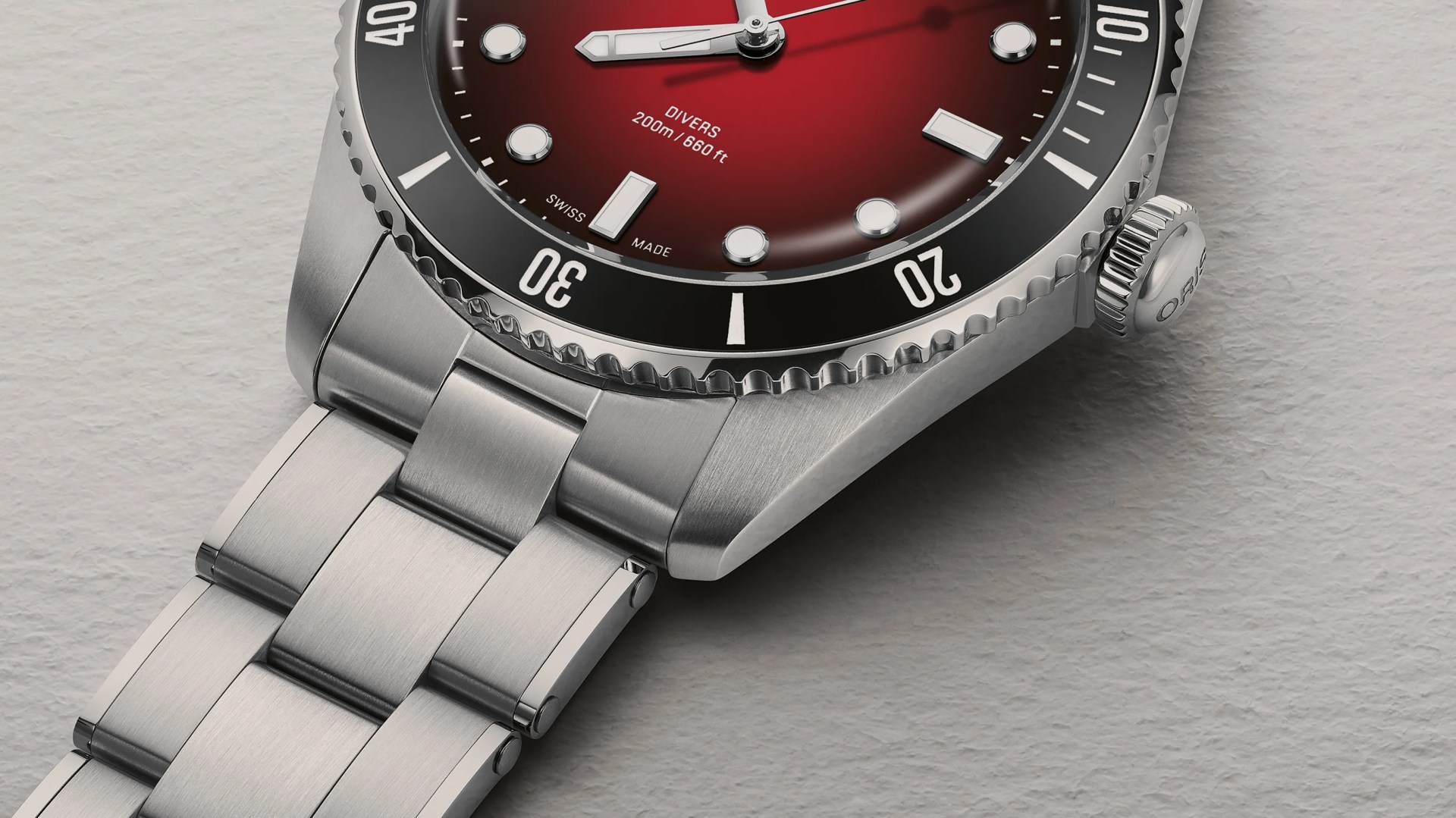 Close-up of a stainless steel diver's watch with a red gradient dial and black bezel on a textured gray surface.