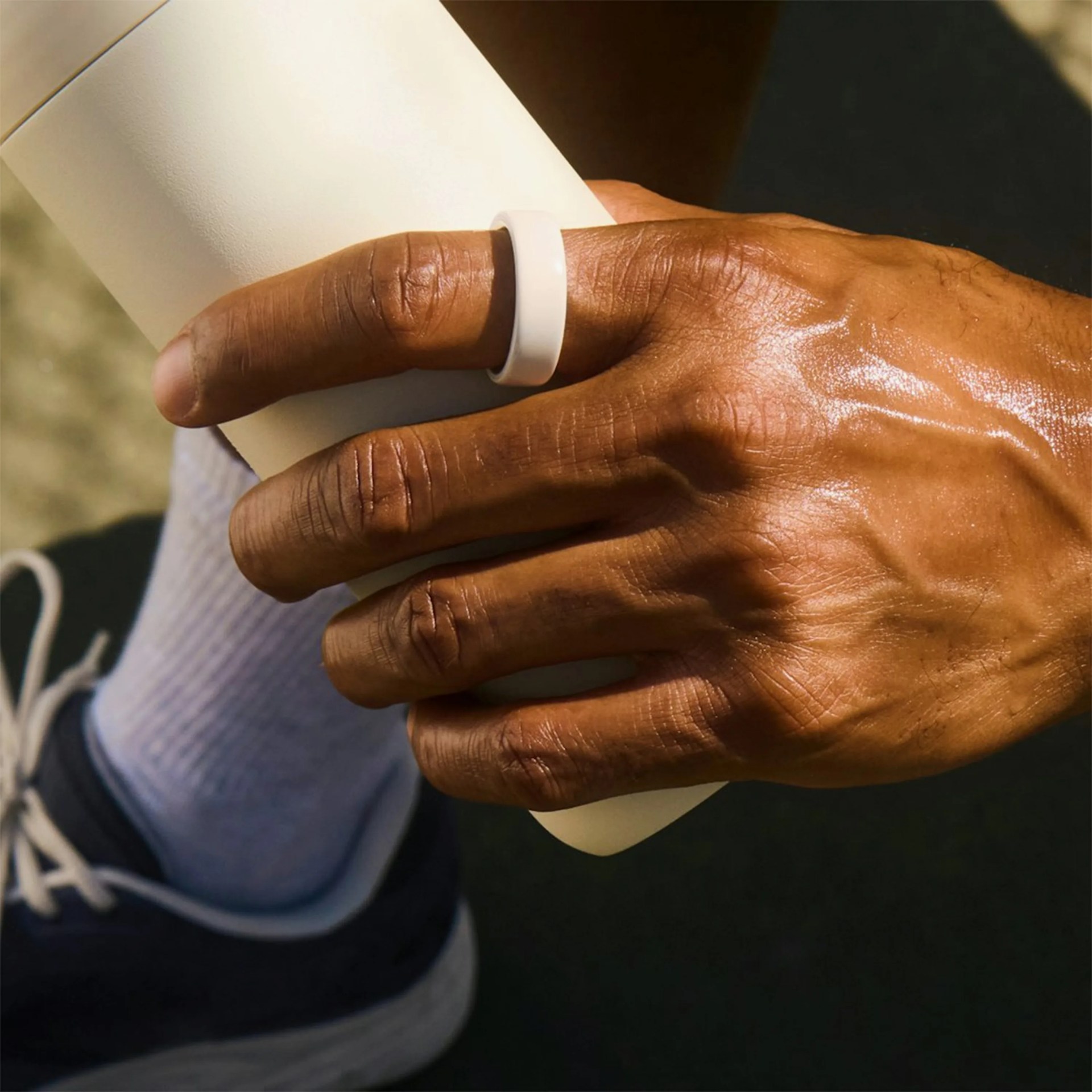 Hand wearing a white silicone ring holding a white cylindrical object, with a sneaker and sock in the background.