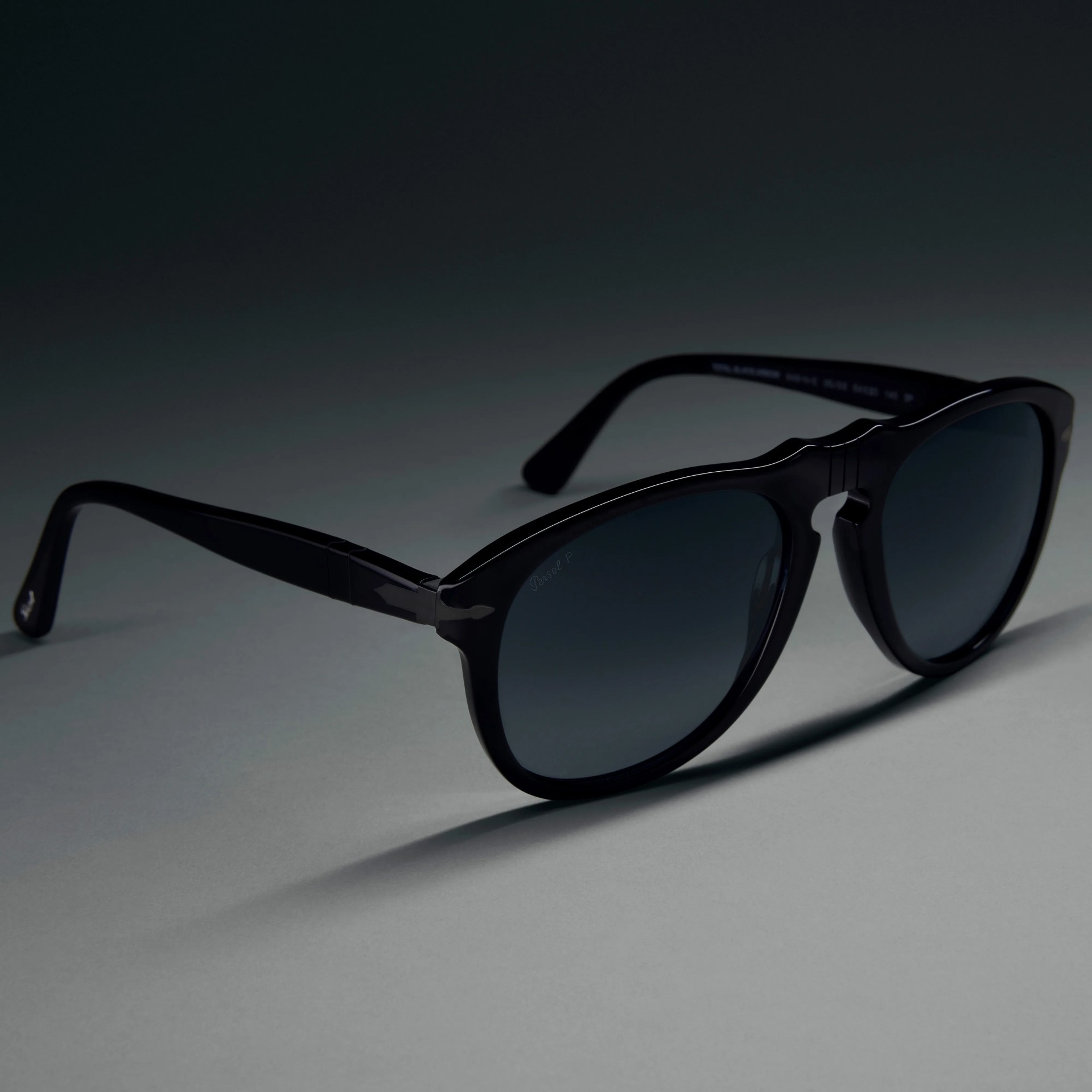 Black acetate sunglasses with dark tinted lenses on a gray surface.