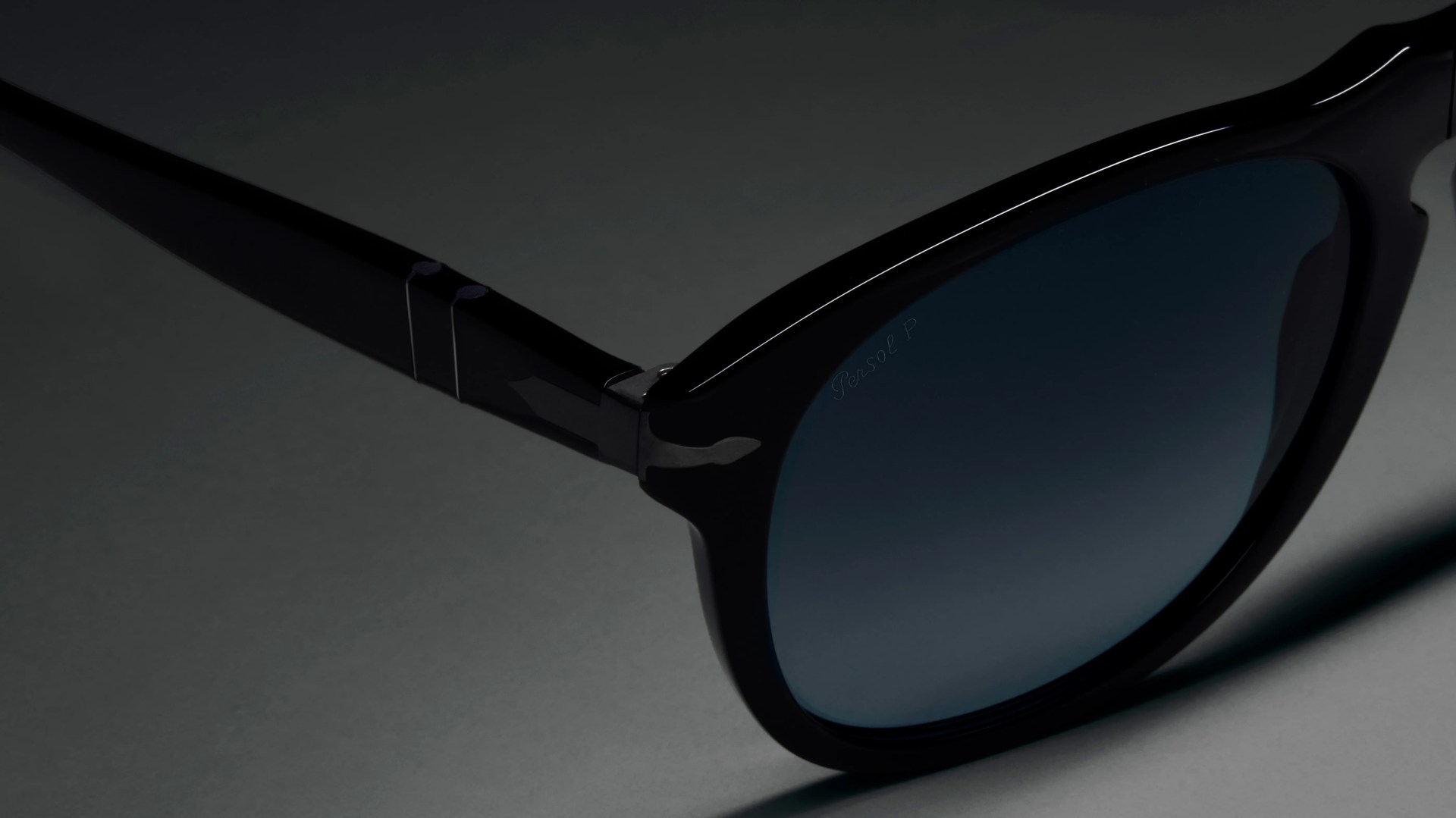 Close-up of black acetate sunglasses with dark tinted lenses on a gray surface.