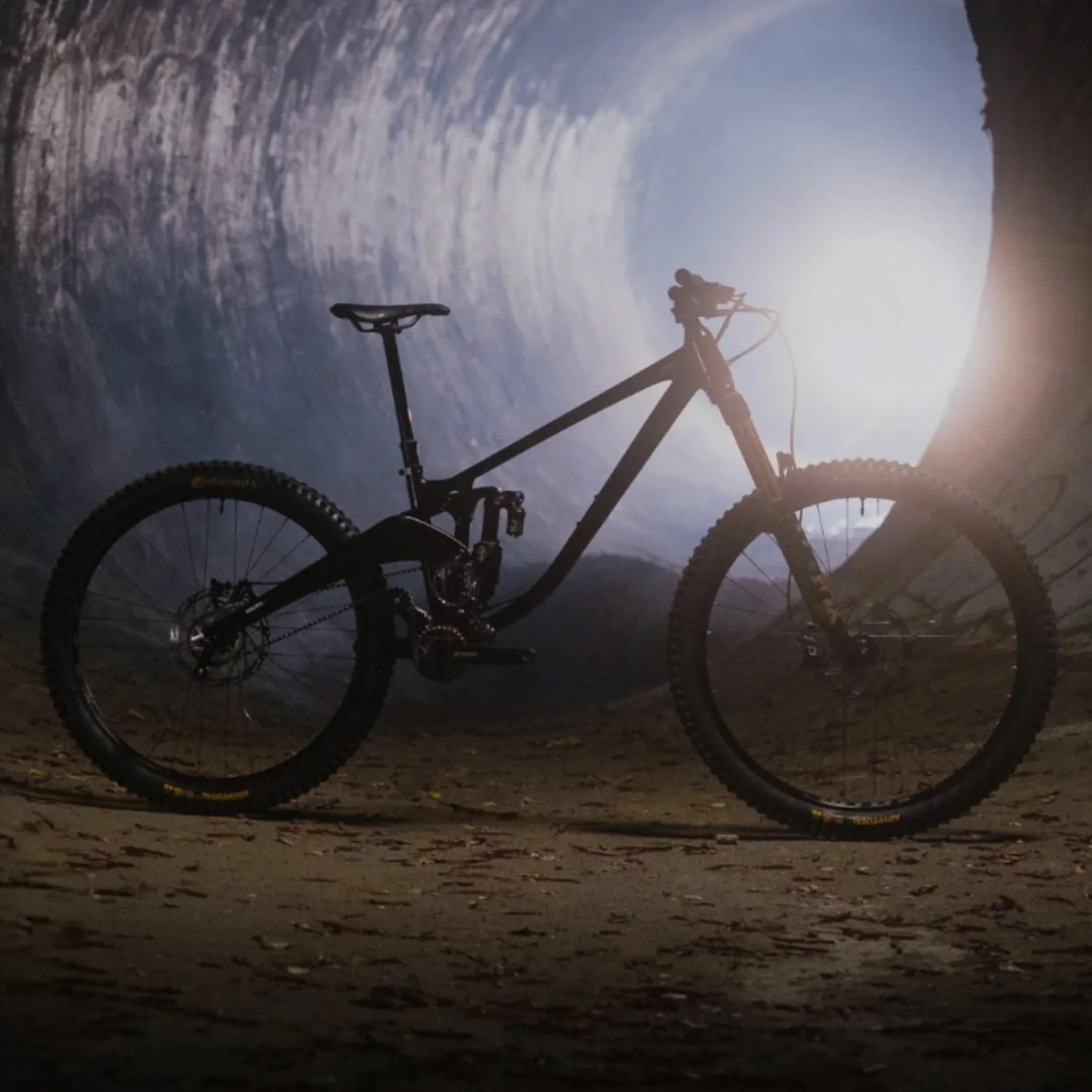 Black full-suspension mountain bike with knobby tires inside a tunnel with light at the end.