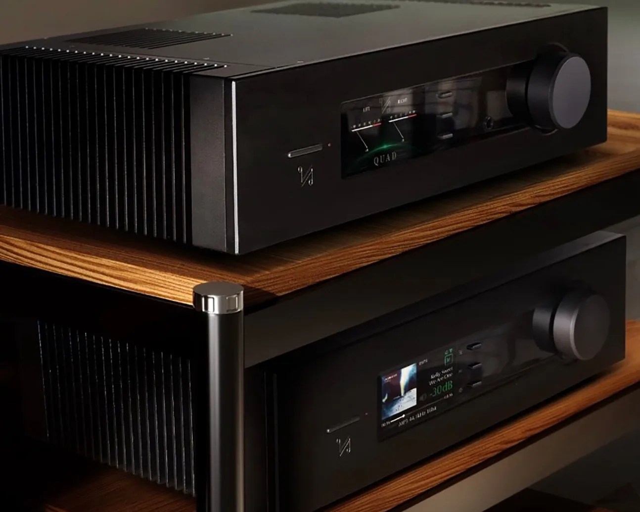 Two black audio amplifier units with digital displays and large control knobs on wooden shelves.