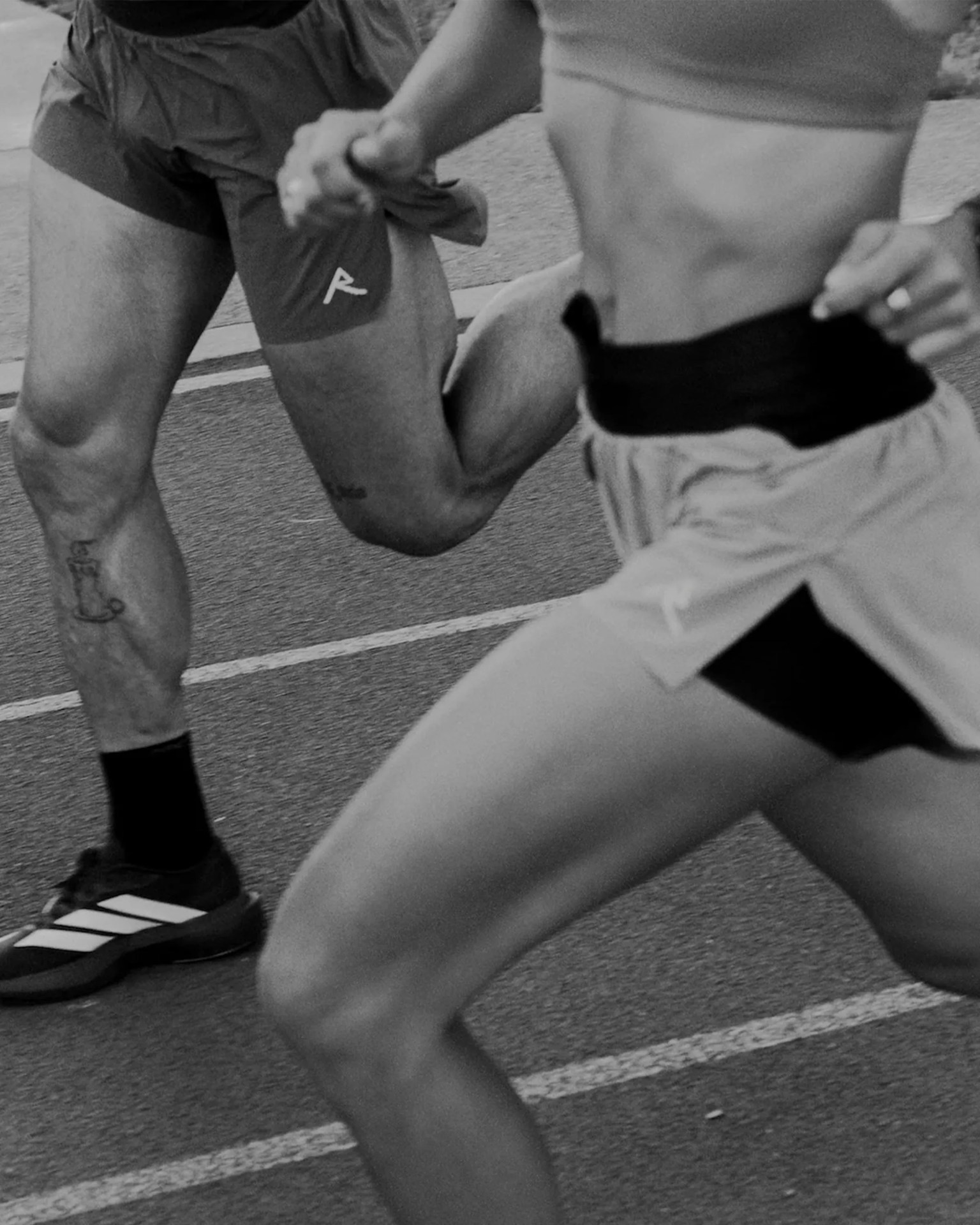 Two runners in shorts sprinting on a track, one wearing Adidas shoes and the other Puma shorts.