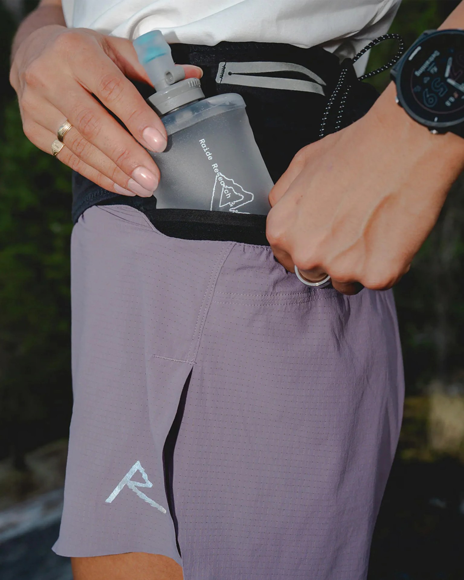 Person placing a translucent Raide Research water bottle into the side pocket of light purple athletic shorts.