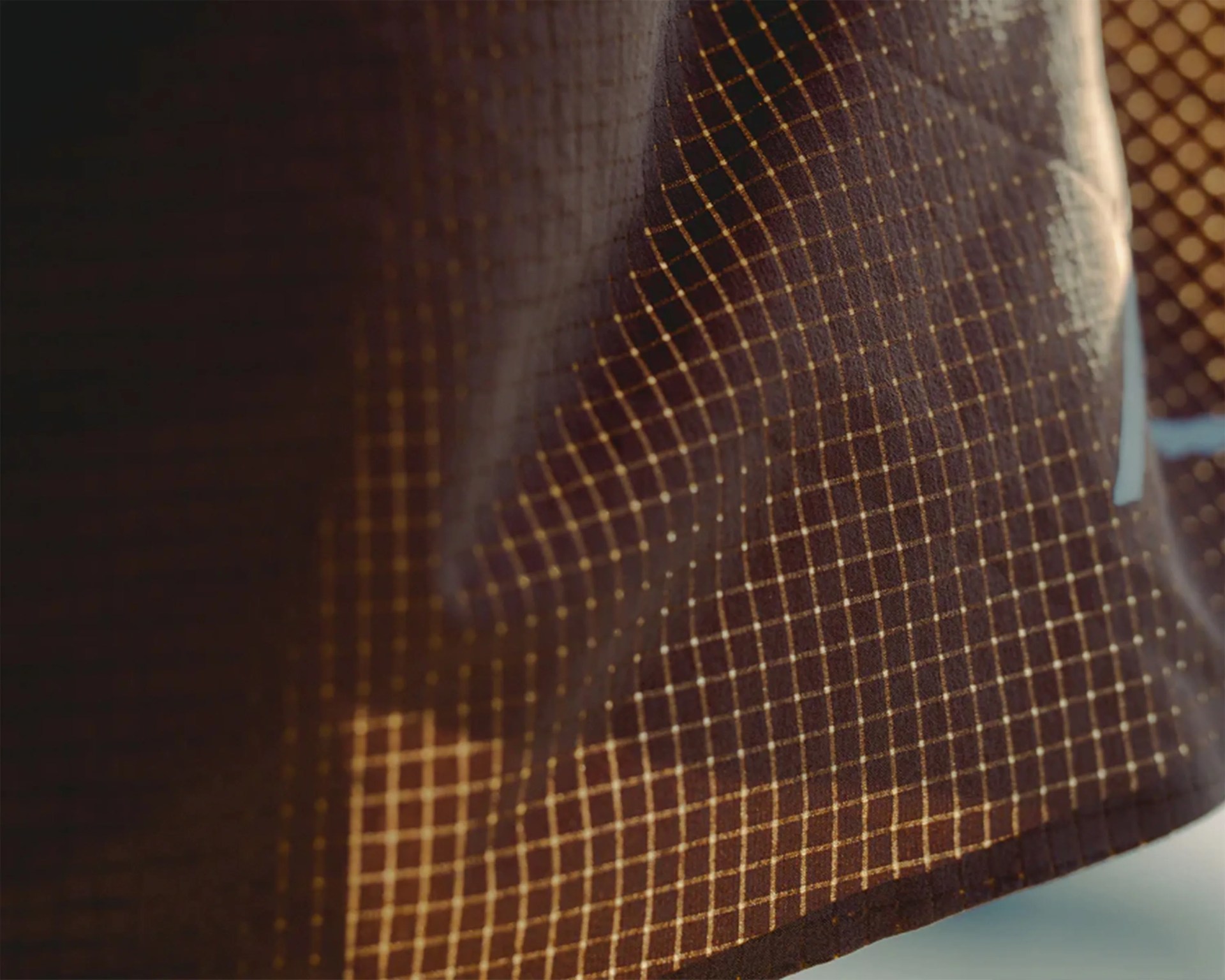Close-up of dark fabric with a grid pattern of thin yellow lines and small dots.