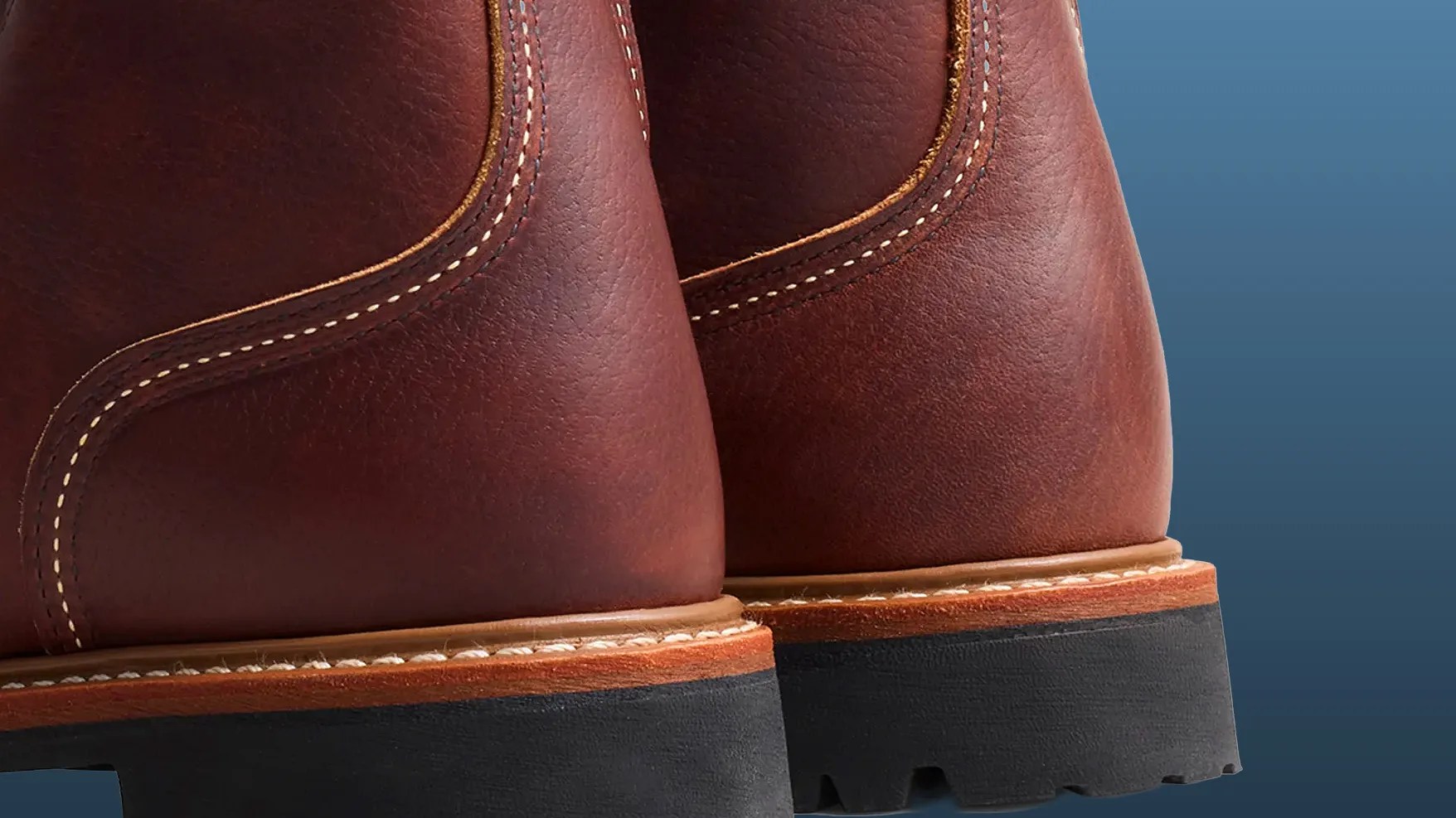Close-up of brown leather boots with detailed stitching and black rubber soles against a blue background.