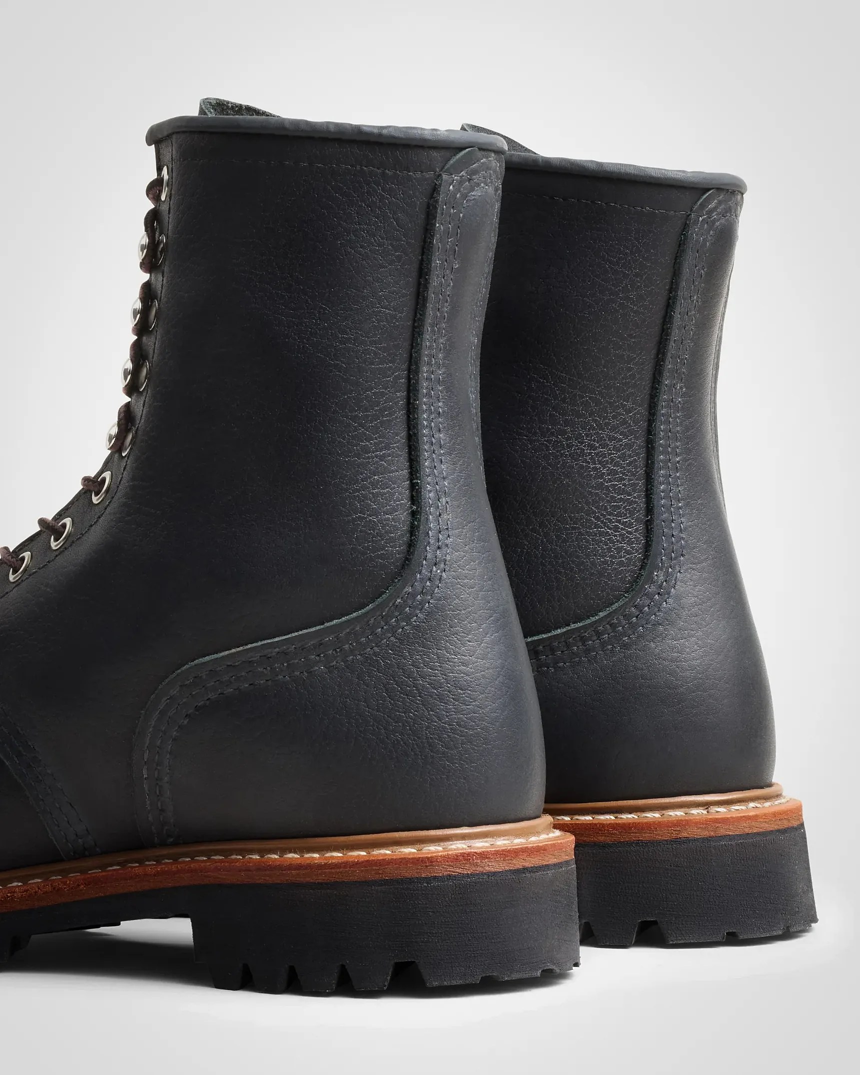 Pair of black leather boots with brown stacked heels and black lug soles shown from the back.