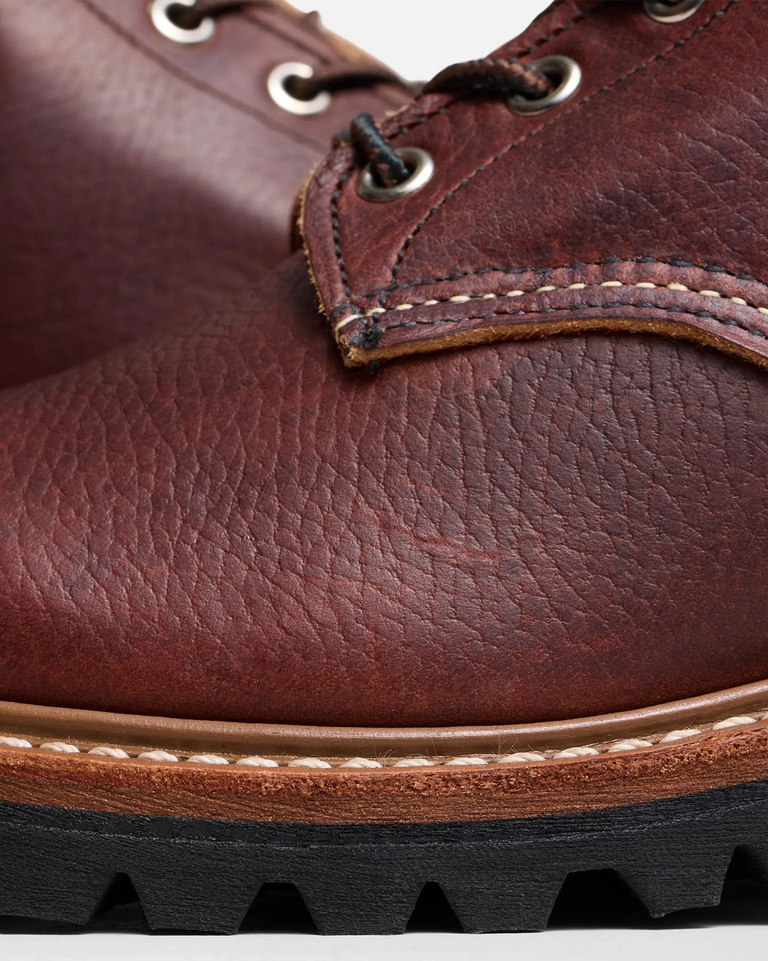 Close-up of a brown leather boot with black laces, detailed stitching, and a black rugged sole.