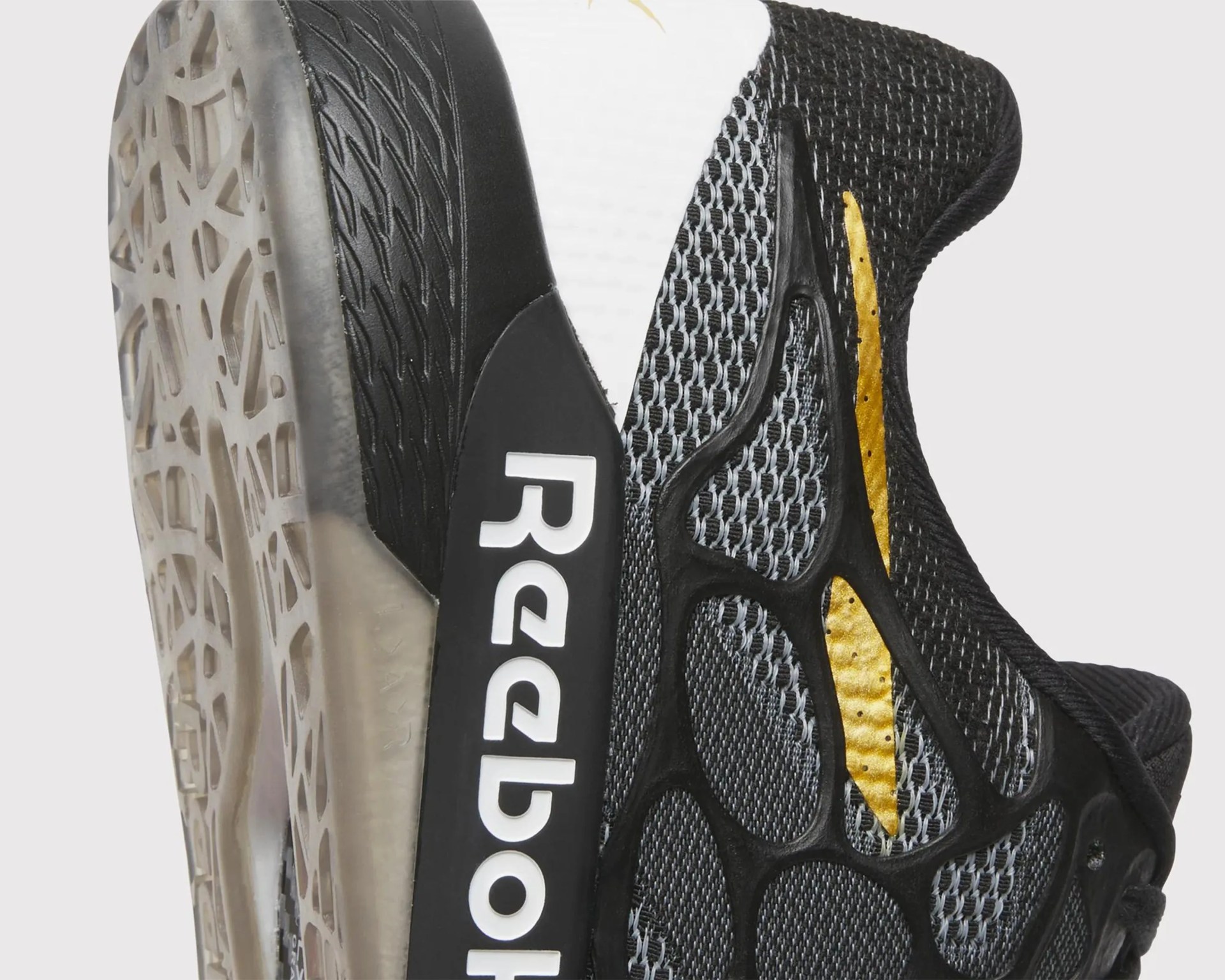 Close-up of a black and gray Reebok sneaker with a gold accent and a translucent patterned sole.