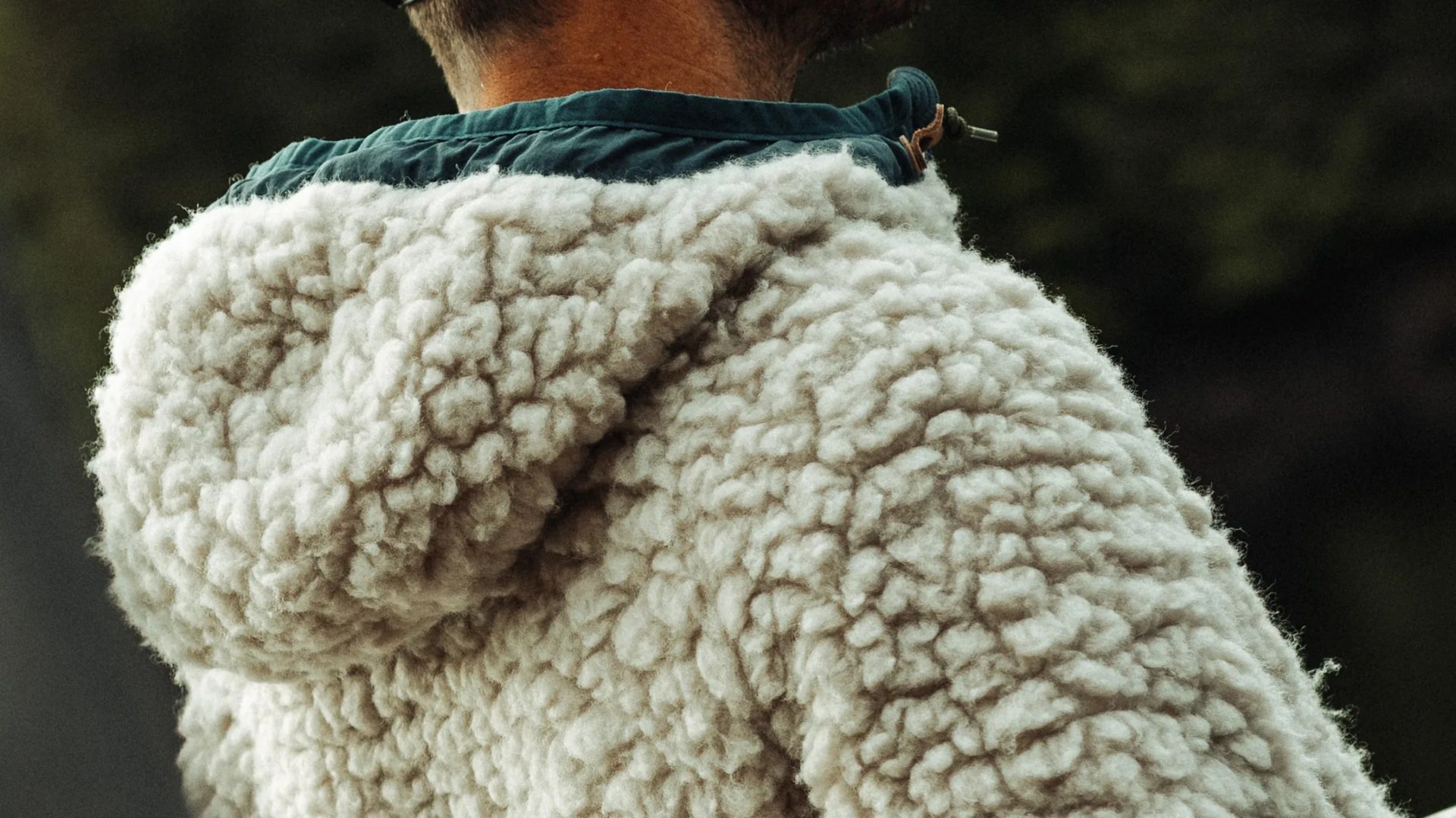 Close-up of a cream-colored sherpa fleece jacket with a teal collar and hood.