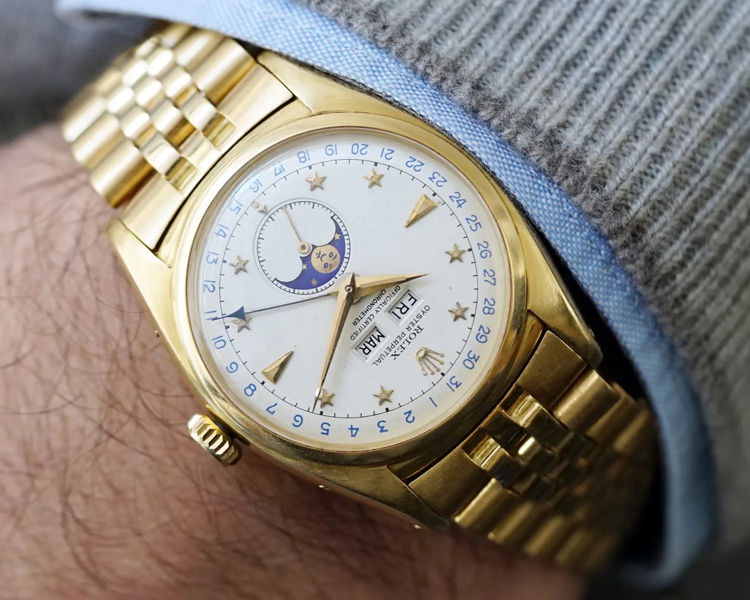 Gold Rolex wristwatch with white dial, star hour markers, moon phase indicator, and day-date display worn on a wrist.
