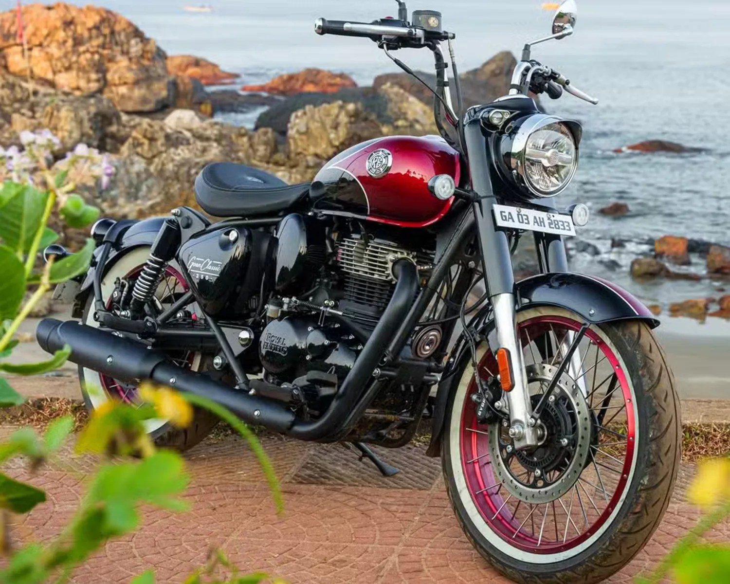Black and red Royal Enfield motorcycle parked on a paved area near rocky coastline.
