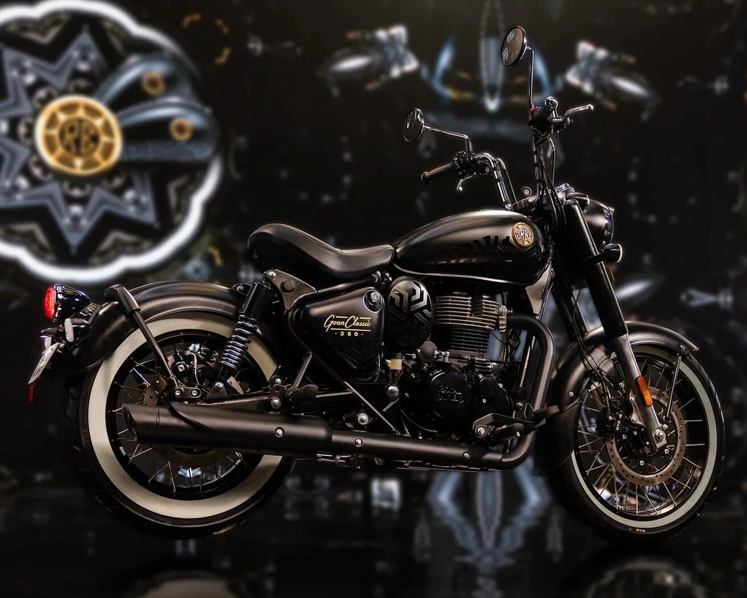 Black Royal Enfield Goan Classic 350 motorcycle with whitewall tires against a dark patterned background.