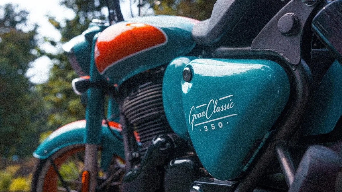 Teal and orange Royal Enfield Goan Classic 350 motorcycle side panel with logo in an outdoor setting.