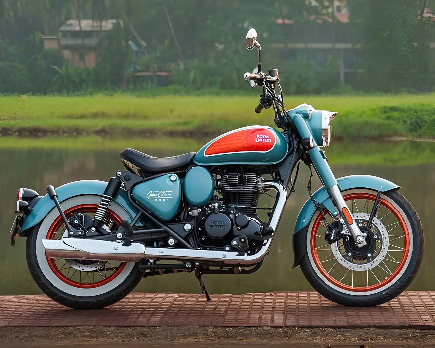Blue and orange Royal Enfield motorcycle with whitewall rear tire parked on a brick surface near water.