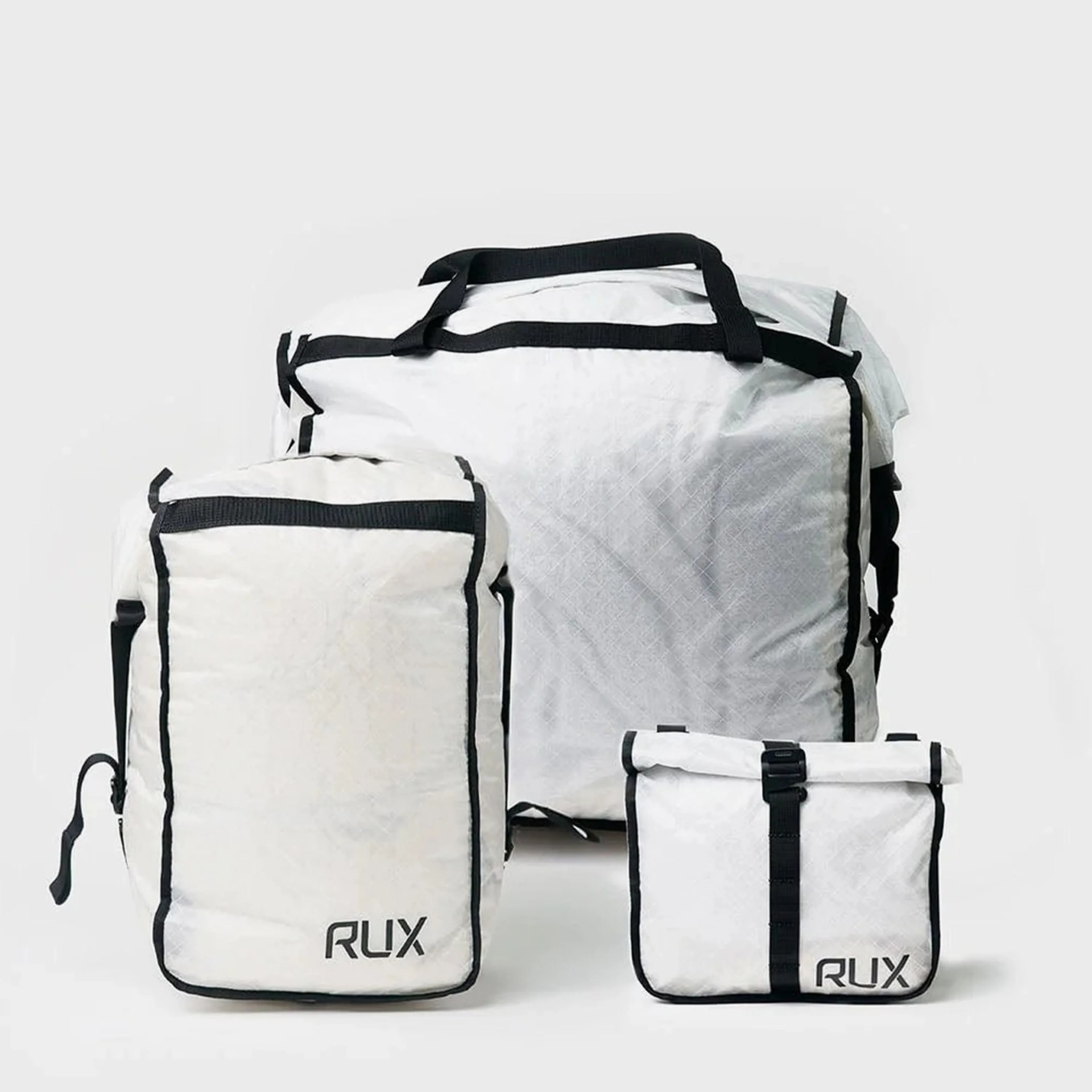 Three white RUX bags with black trim, including a large duffel, a rectangular backpack, and a small roll-top pouch.