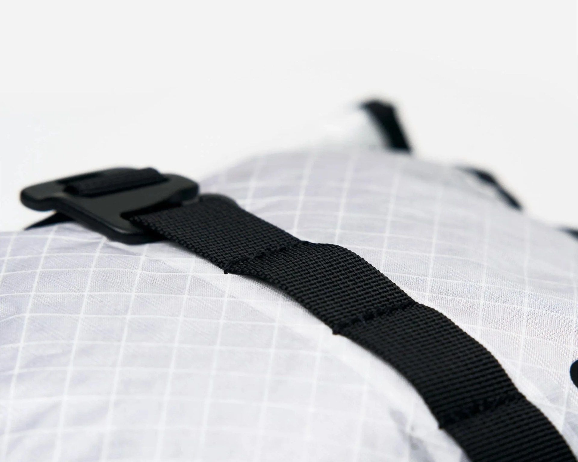 Close-up of a black nylon strap with a plastic buckle on a white fabric with a grid pattern.