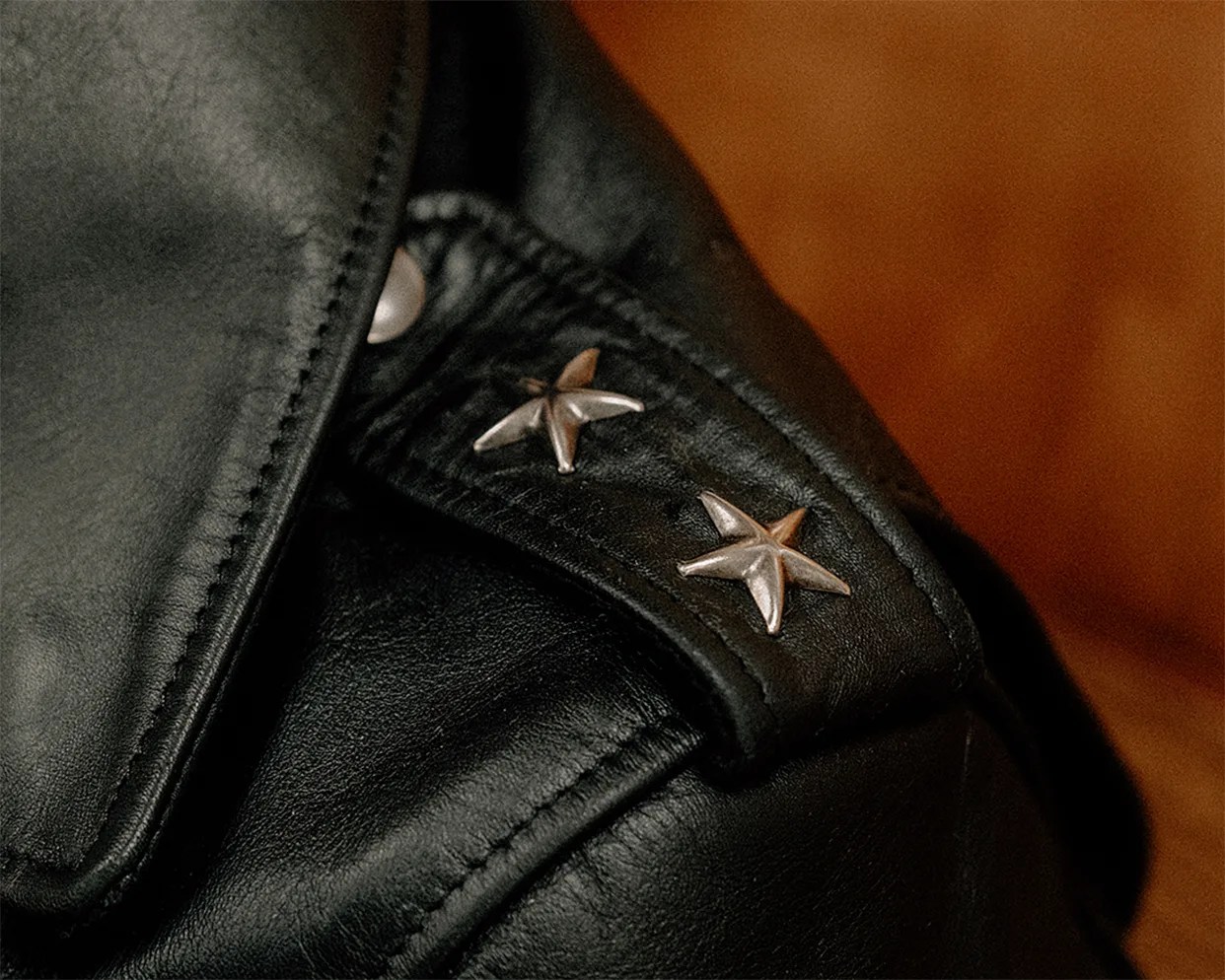 Close-up of black leather jacket shoulder with two silver star-shaped studs.