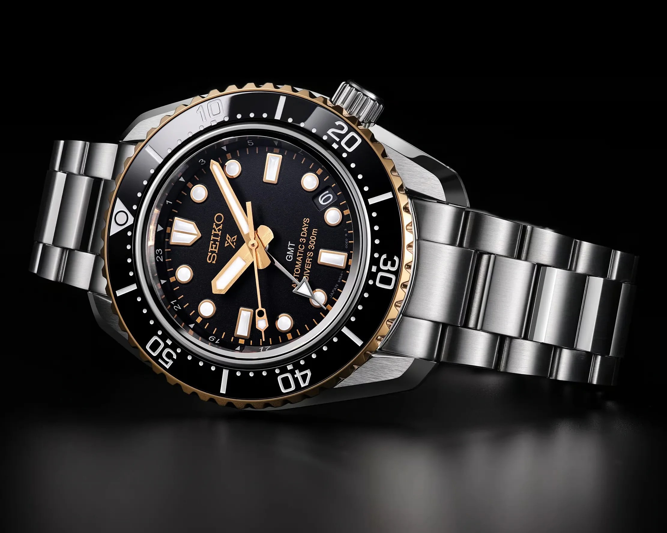 Seiko Prospex GMT diver's watch with black dial, gold accents, and stainless steel bracelet on black background.