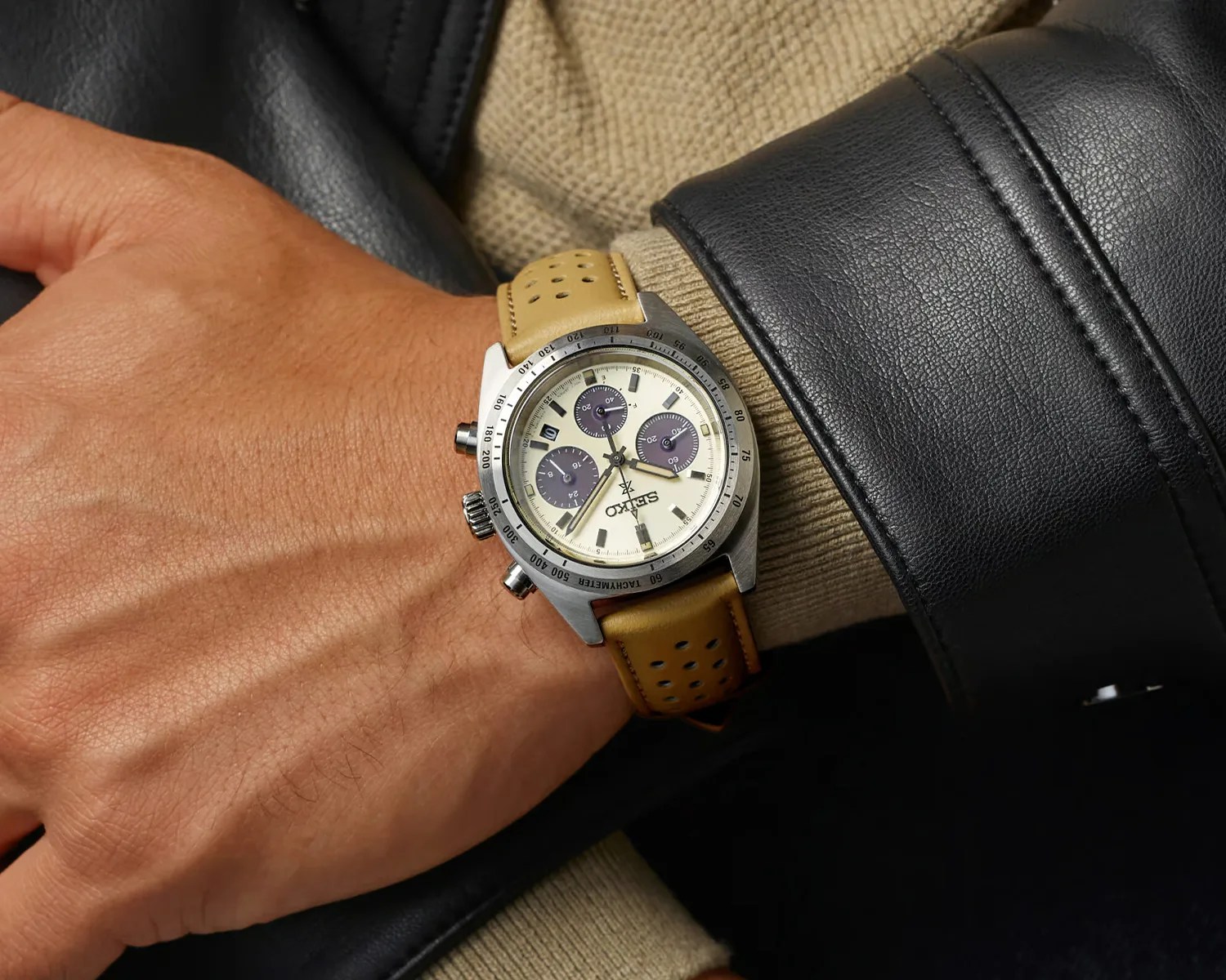 Seiko chronograph watch with cream dial, three dark subdials, and perforated tan leather strap on a wrist.