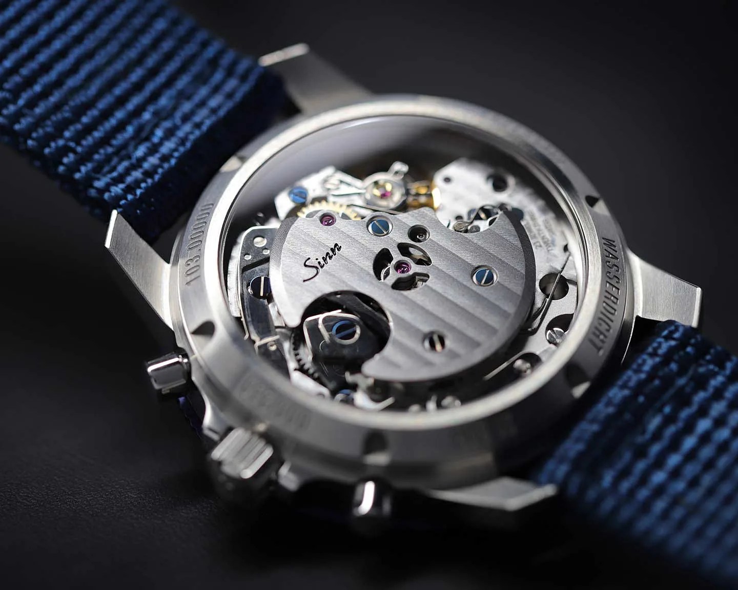 Close-up of the back of a Sinn mechanical watch with visible movement and a blue fabric strap.