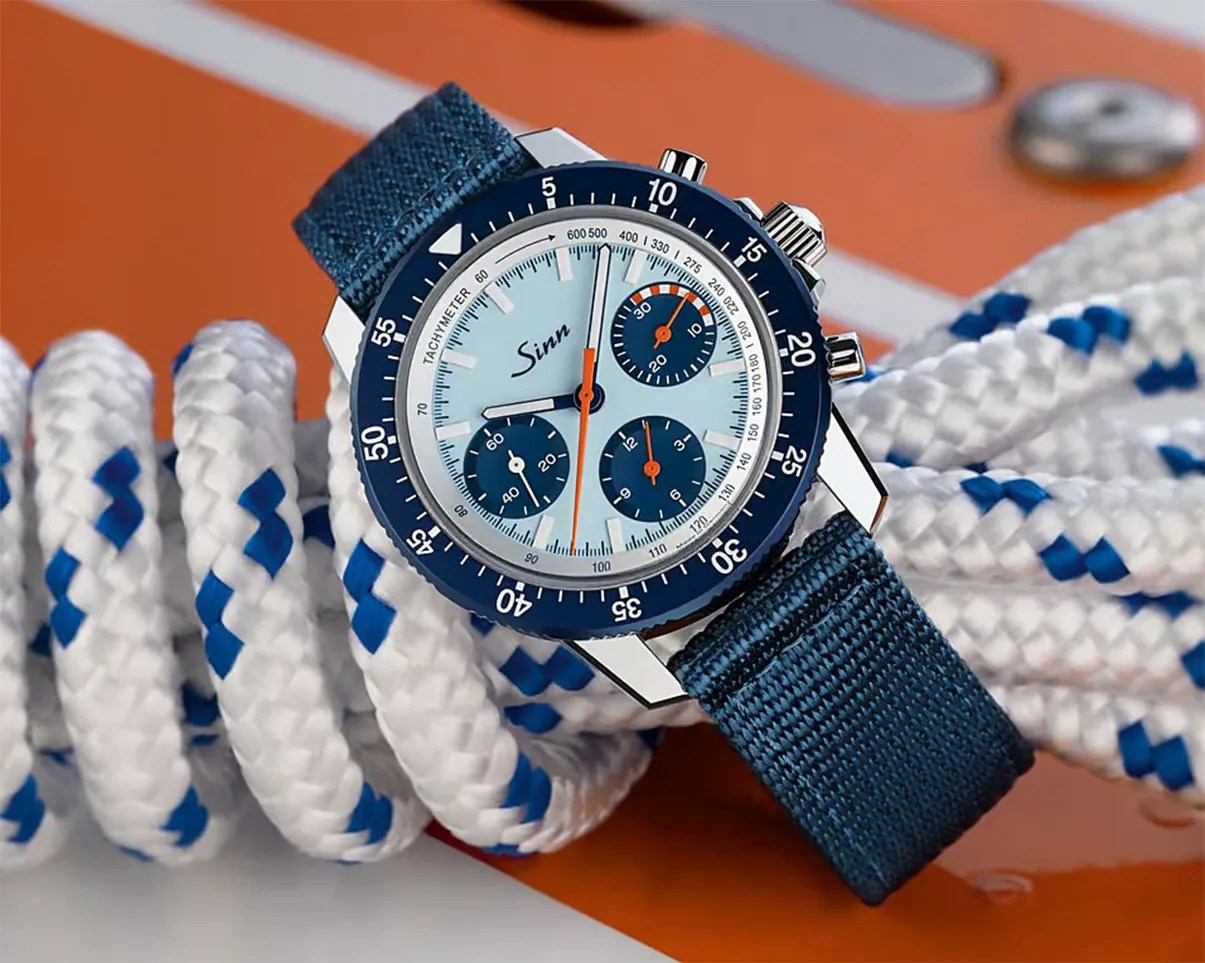 Blue Sinn chronograph watch with white dial, orange accents, and blue fabric strap resting on coiled white rope with blue details.